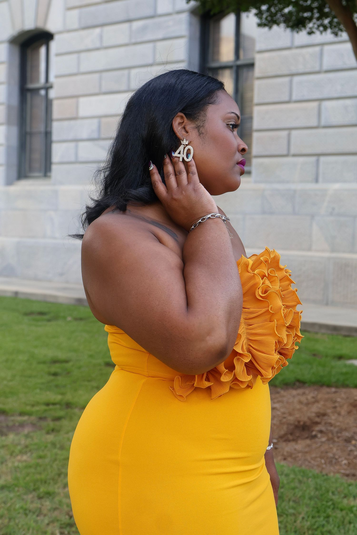 Bright yellow strapless dress with ruffled detail photographed against a stone building exterior.