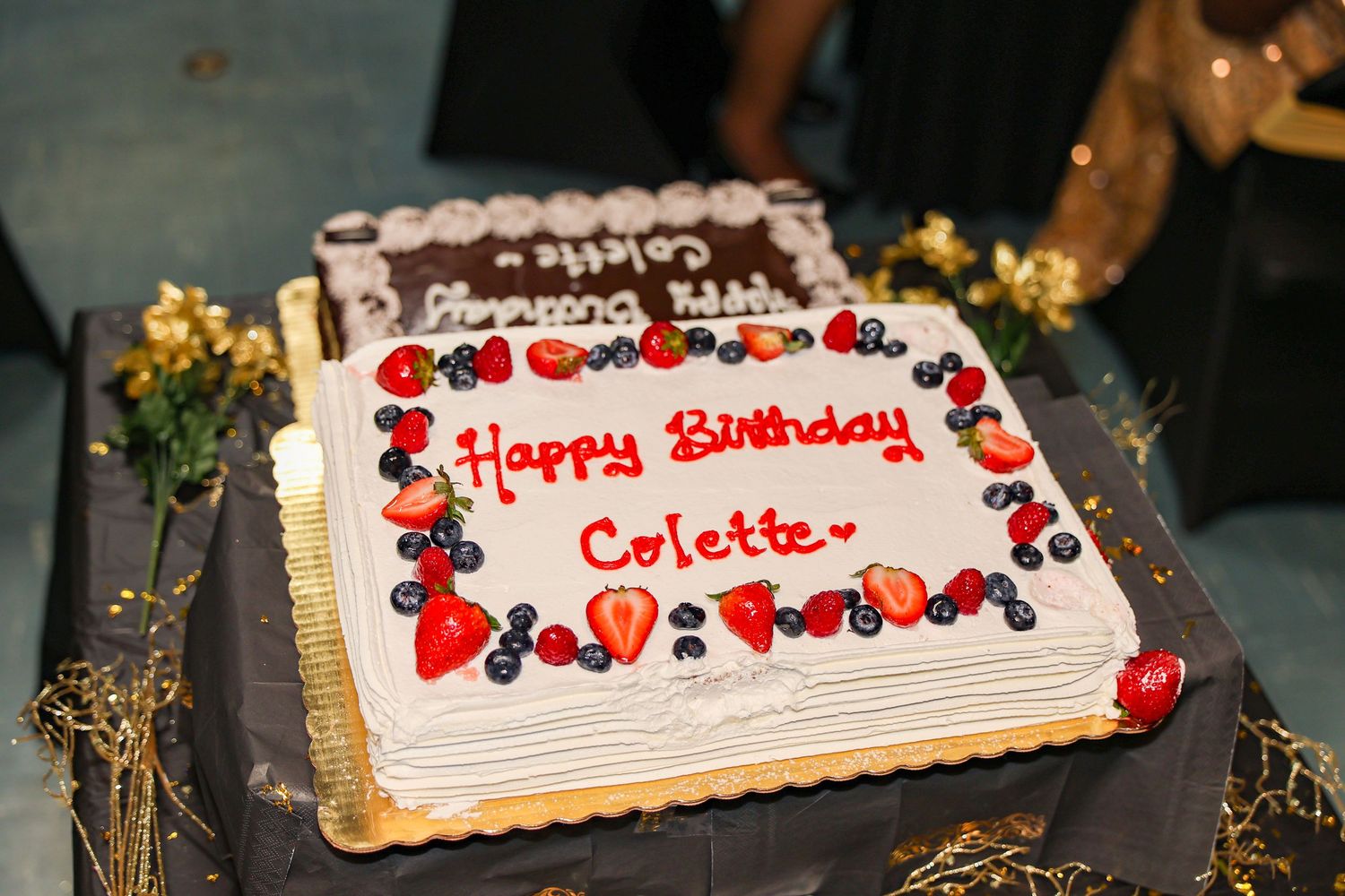 A square white birthday cake decorated with red berries and 'Happy Birthday' written in frosting.