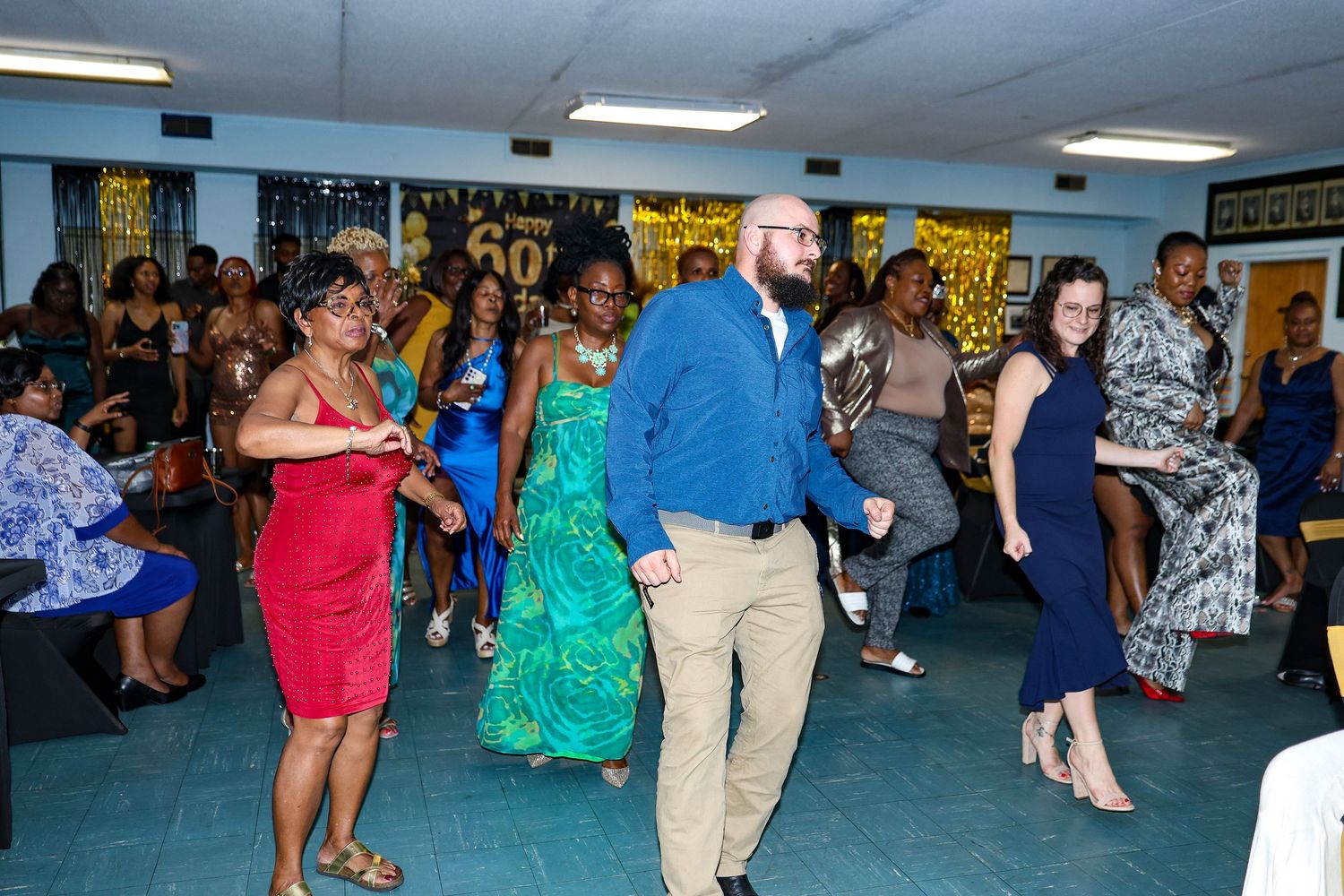 Large group of party guests dancing and mingling in a spacious venue with bright lighting.