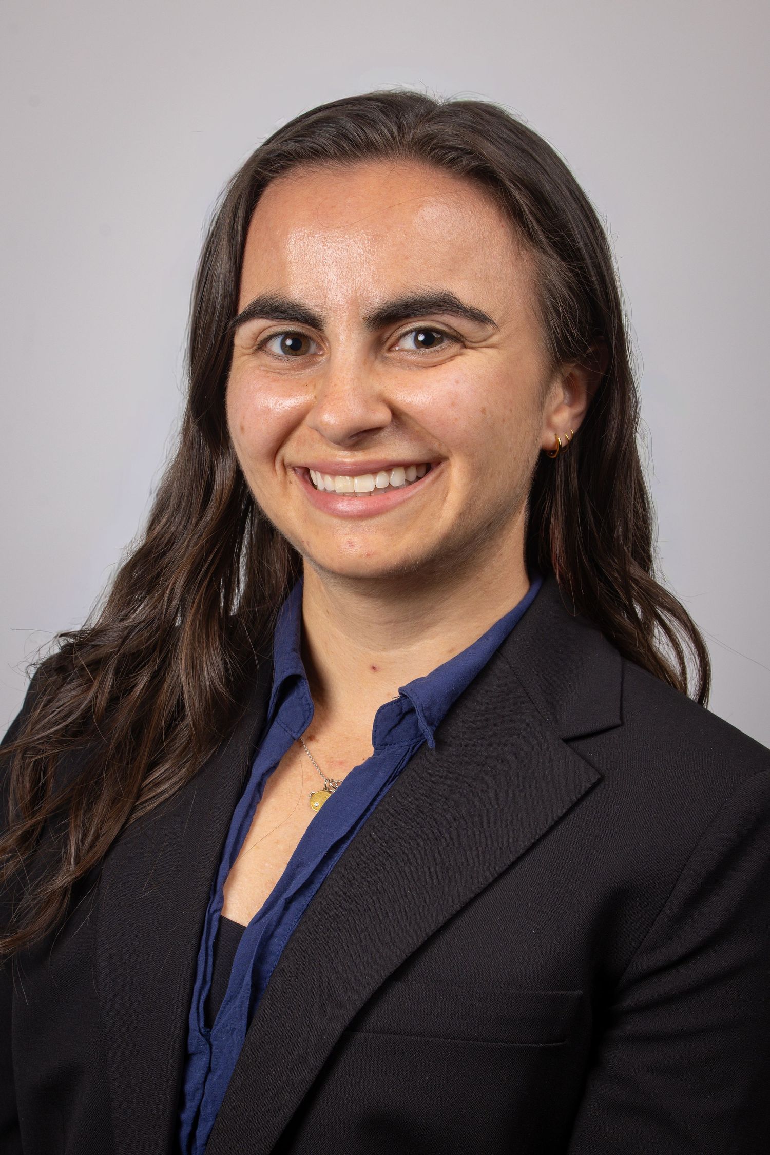 Professional headshot of a smiling young woman with long dark hair wearing a black blazer and blue blouse.