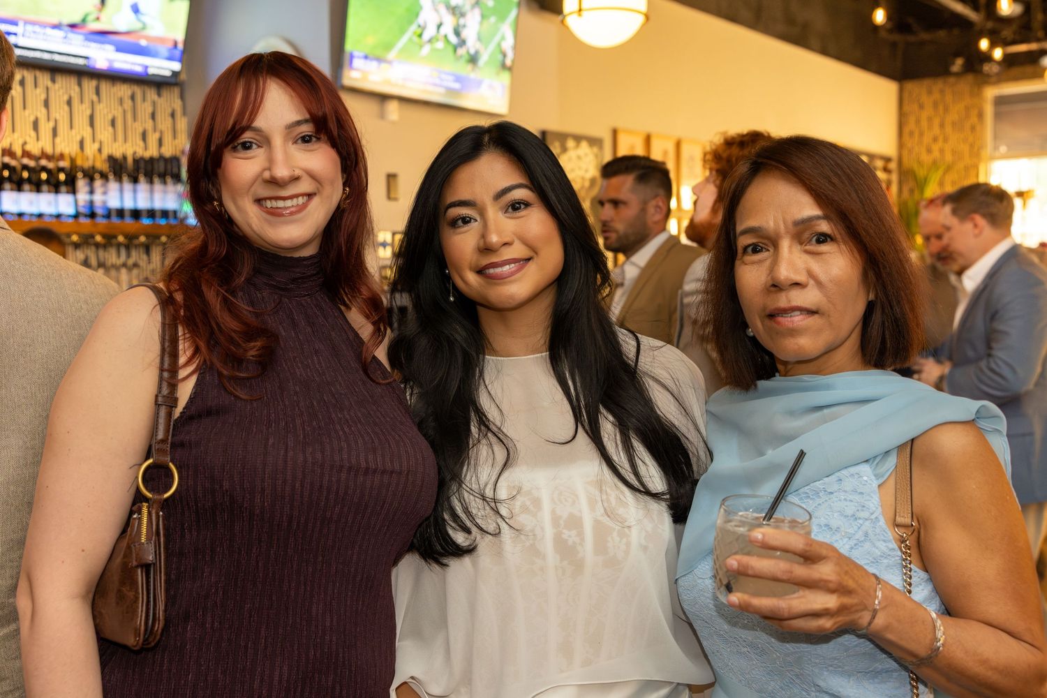 Three women smiling together at an indoor social gathering event.