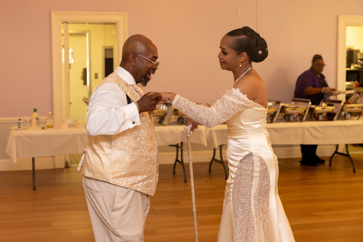 Bride and groom dance together at wedding reception, groom holding a cane in formal attire.