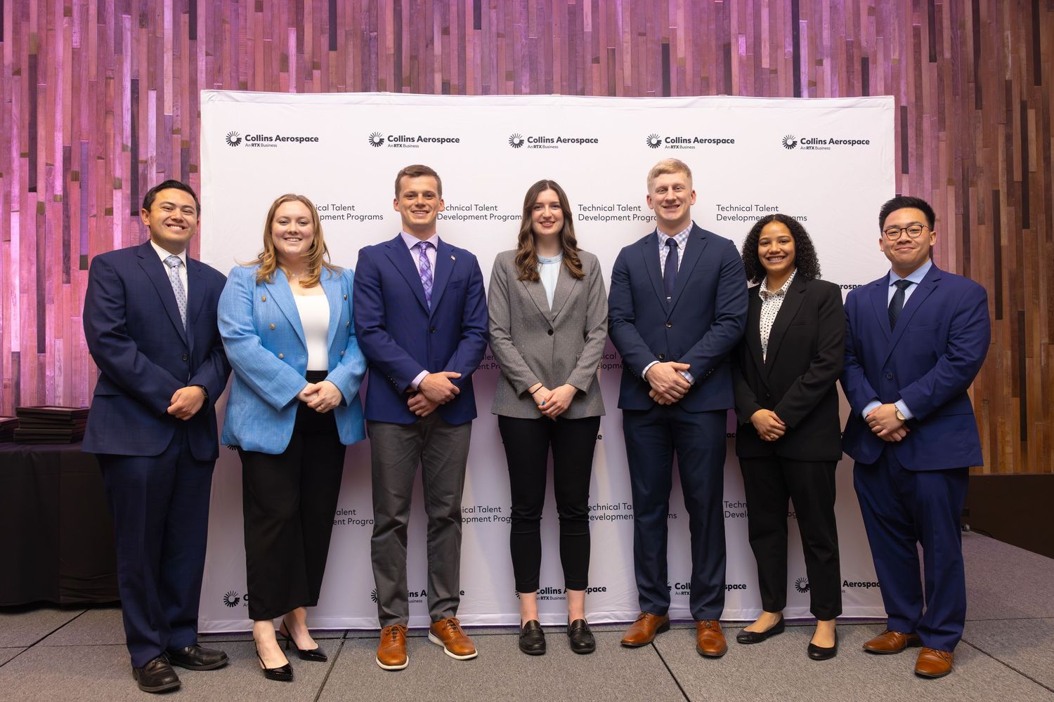 Seven professionals pose together in front of a Collins Aerospace Technical Talent Development Programs backdrop.