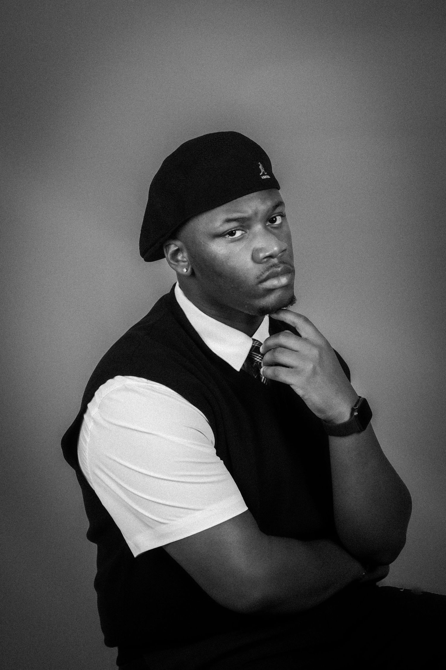 Black and white portrait of a young man in a beret and vest, posing thoughtfully with hand on chin.