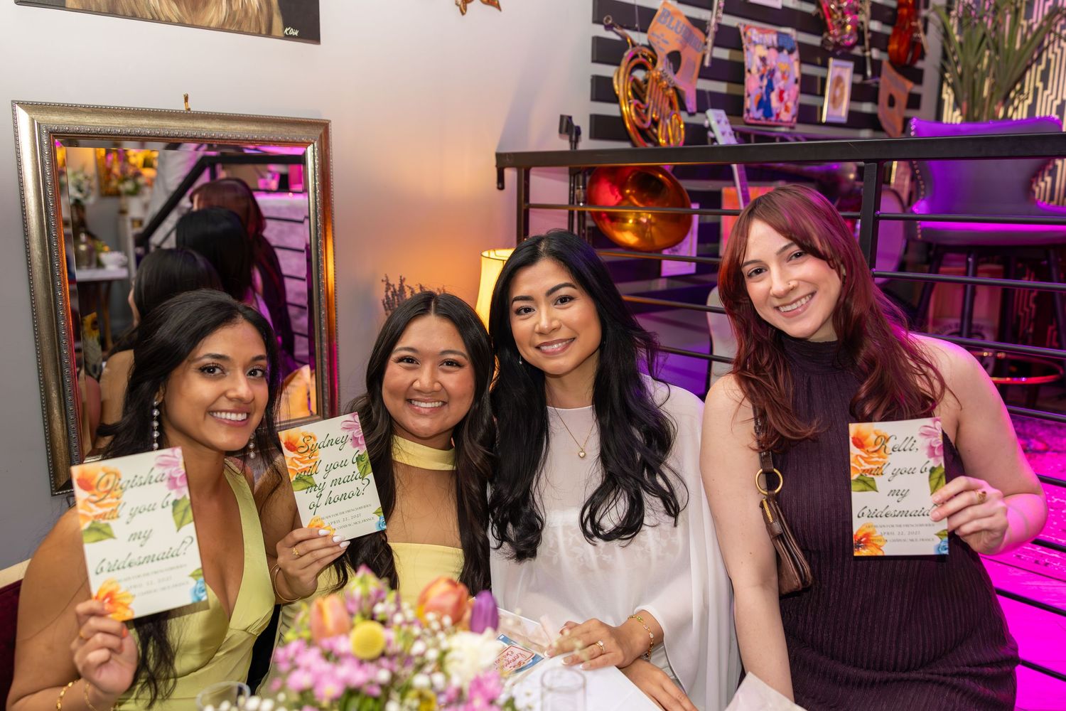 Four young women posing together holding event programs at a party.