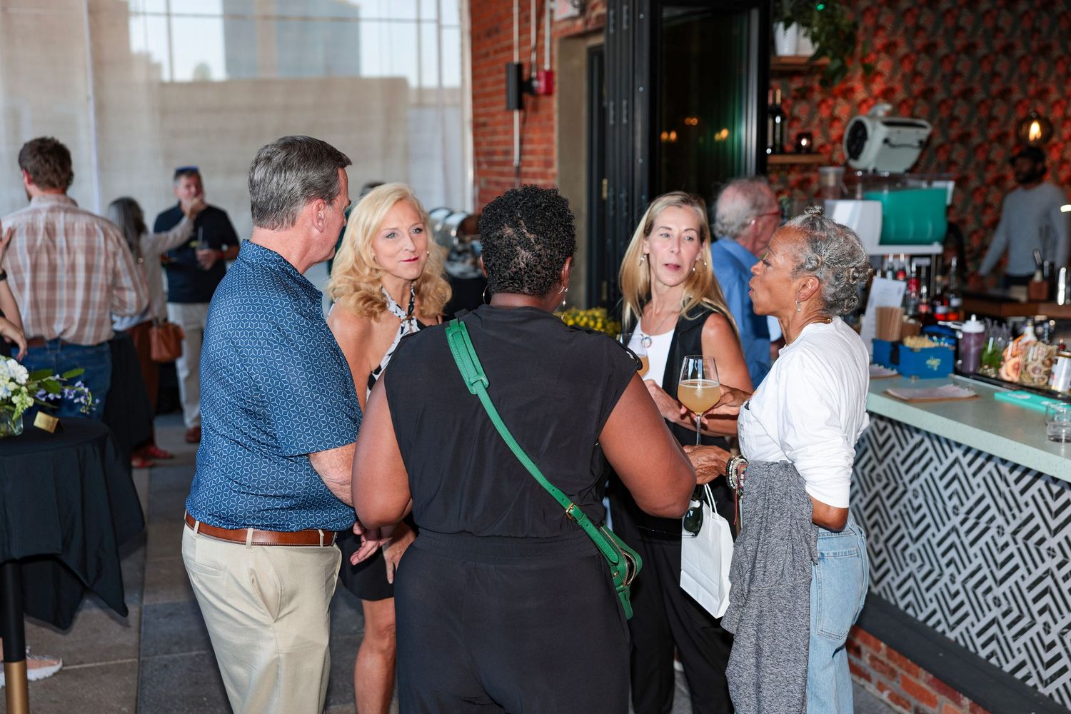 Event attendees socializing near a bar area in a rustic brick venue with string lights.