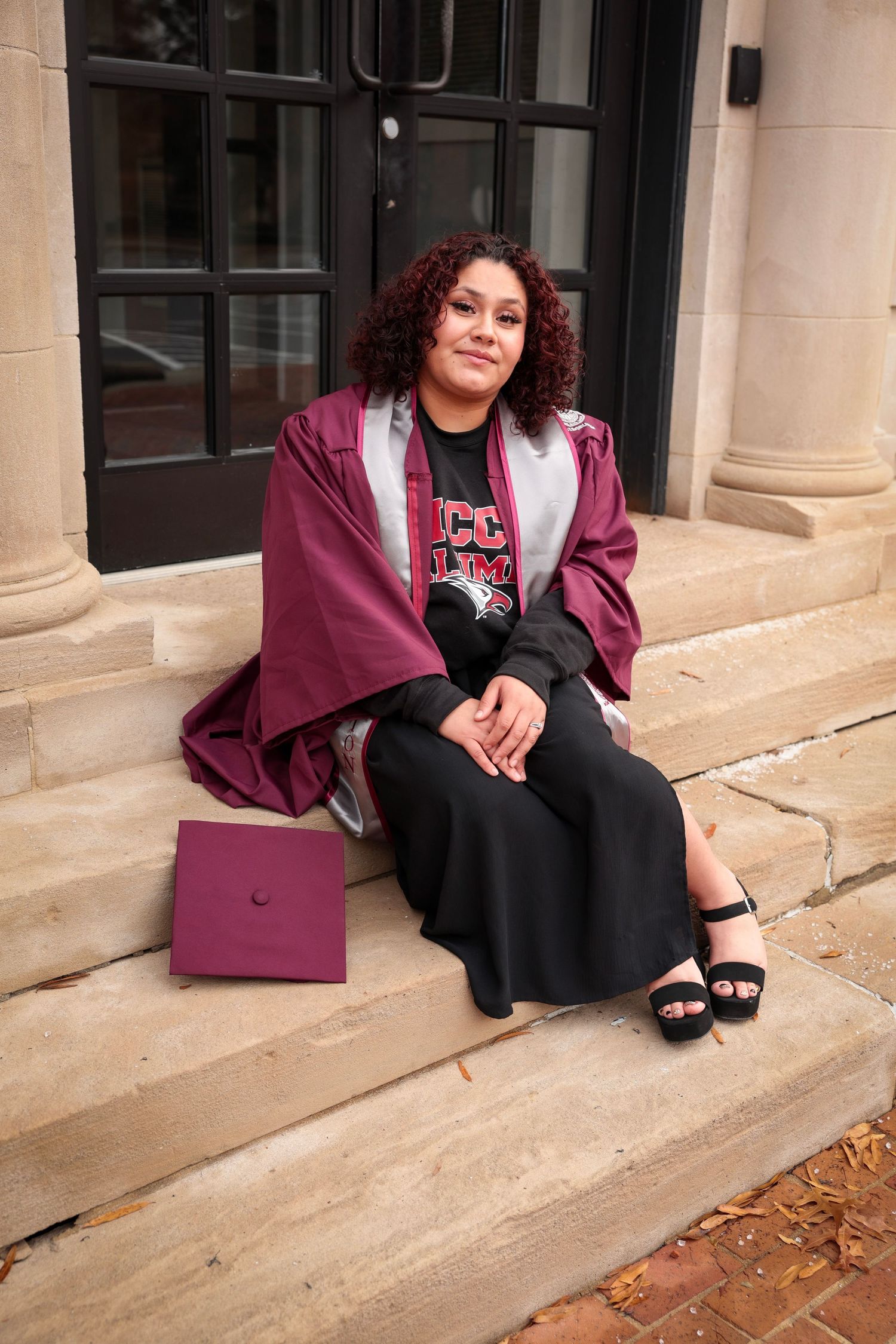 Graduate in burgundy regalia seated on stone steps during photo session.
