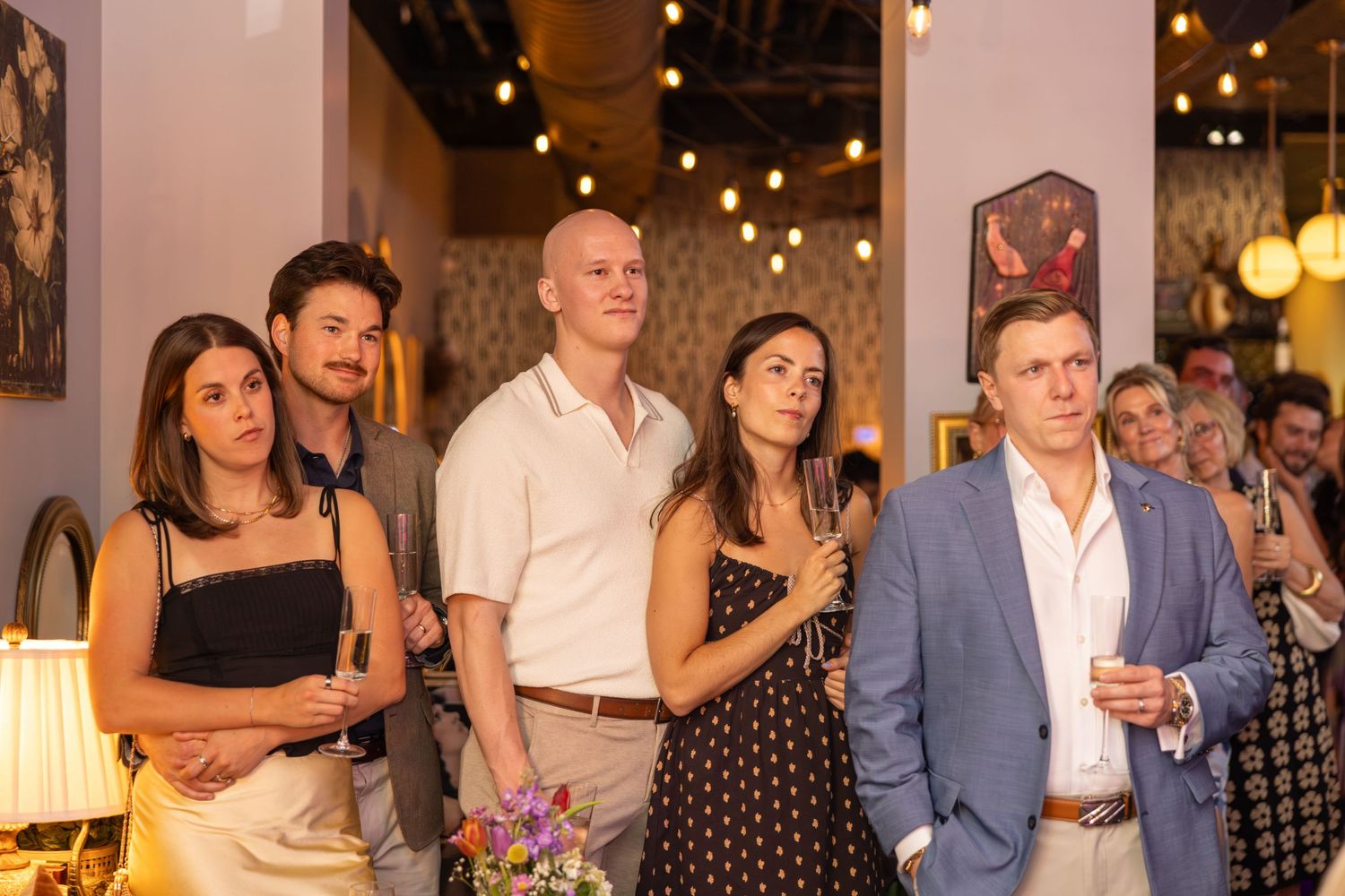 Group of five adults standing together at an indoor social gathering with warm string lights.