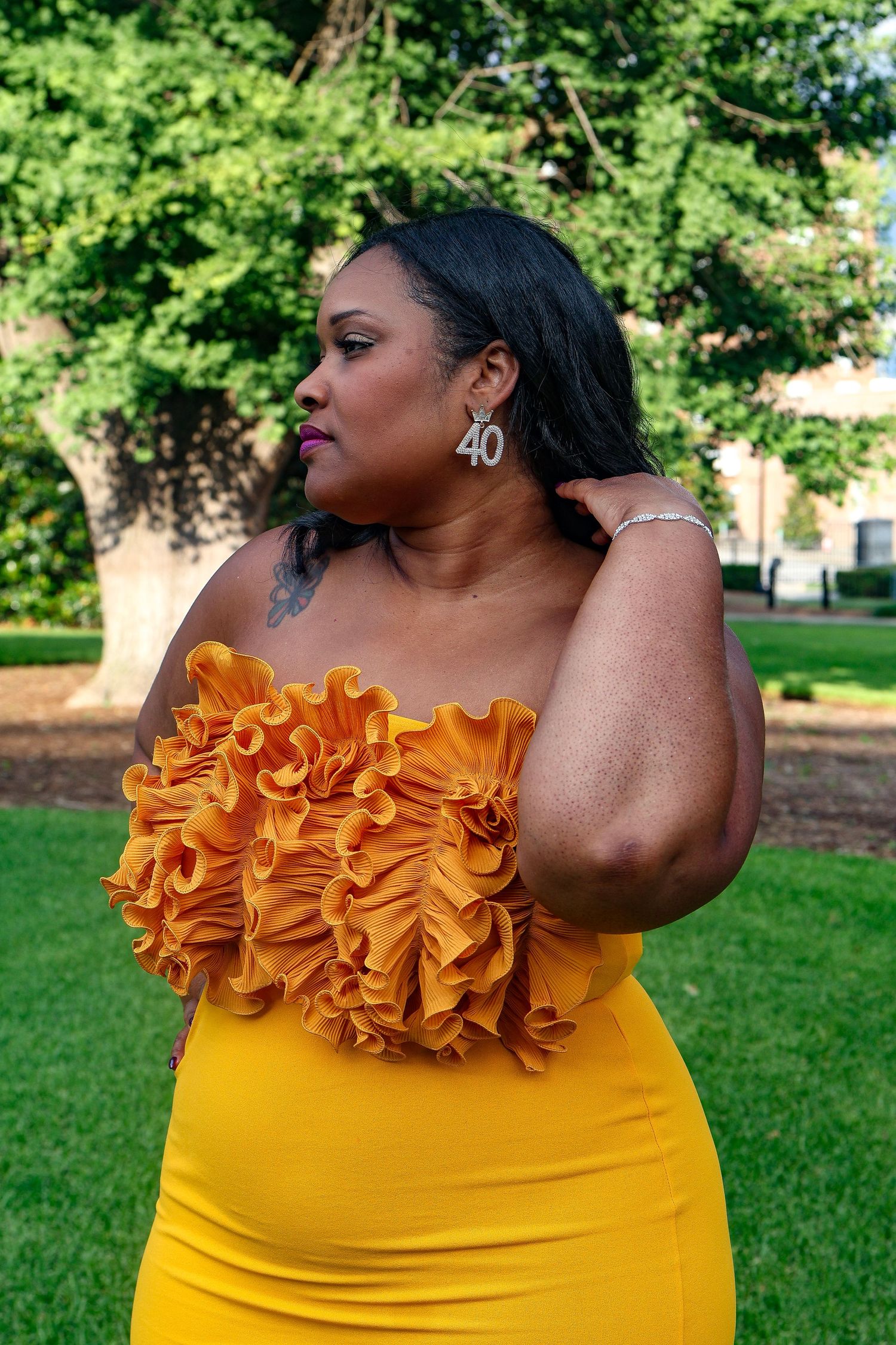 Fashion shoot featuring yellow form-fitting dress with ruffled neckline in outdoor garden setting.