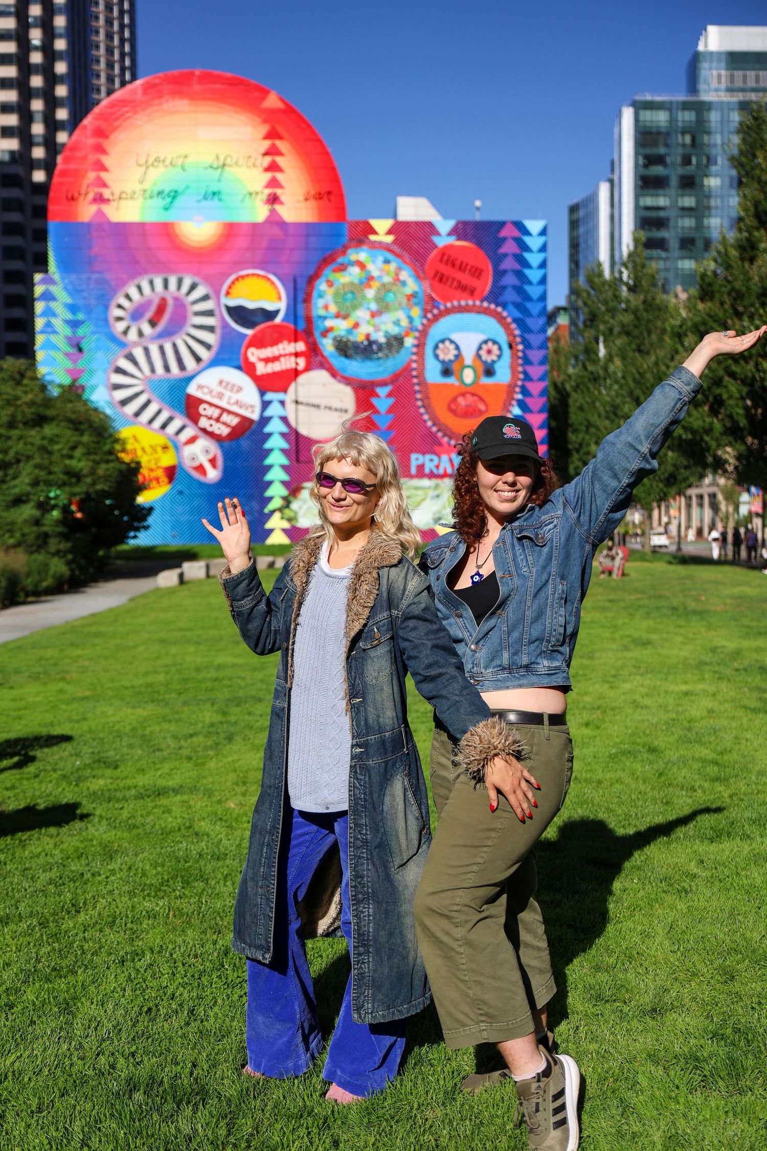 Group poses enthusiastically in front of a rainbow-colored street art mural on green grass.