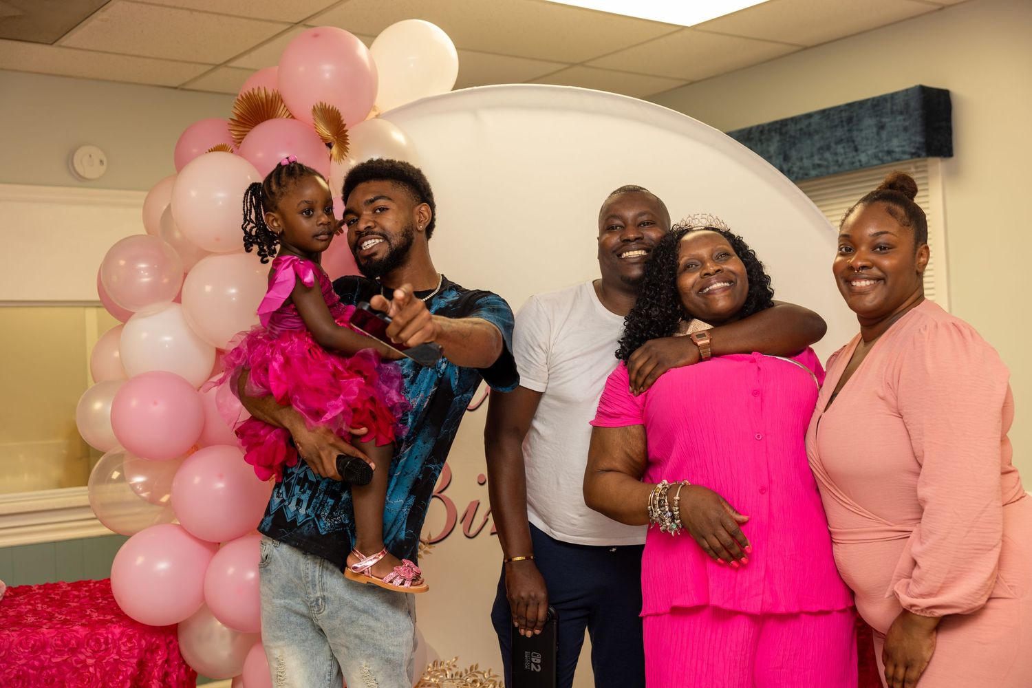 Family celebrating a baby shower with pink balloons and decorations, posing together for a photo.
