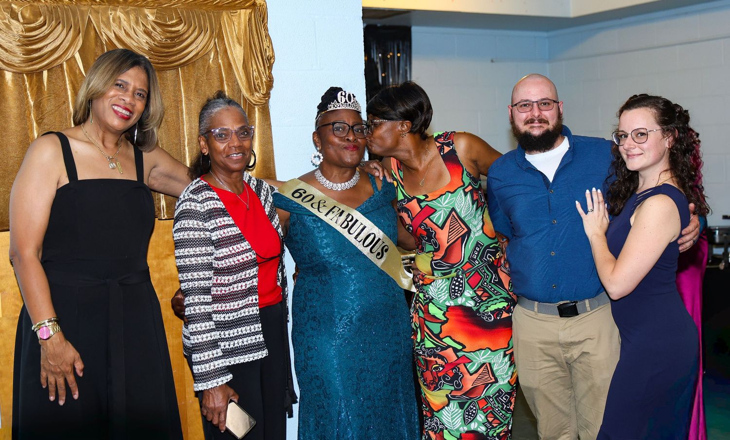 A group photo at a celebration with the guest of honor wearing a teal dress and tiara in the center.
