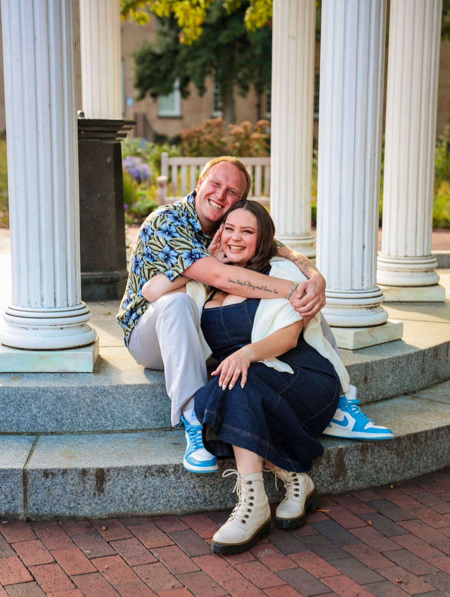 Couple relaxing together between white columns on brick patio.