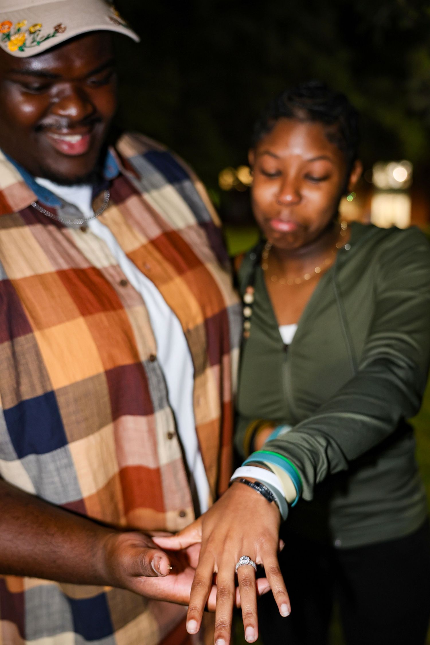 Close-up of hands showing off an engagement ring during a nighttime proposal.