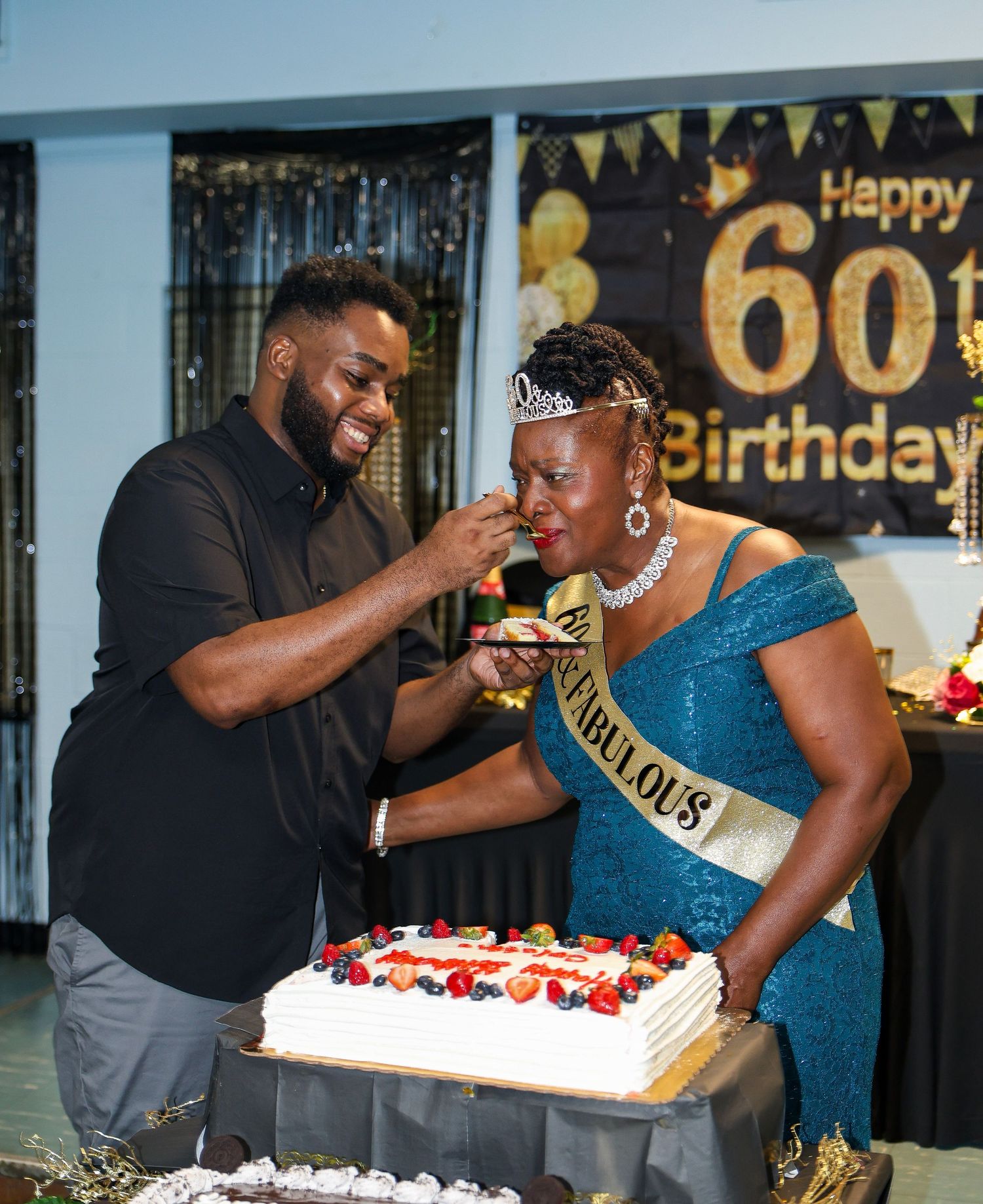 A joyful moment captured as two people share cake at a 60th birthday celebration.
