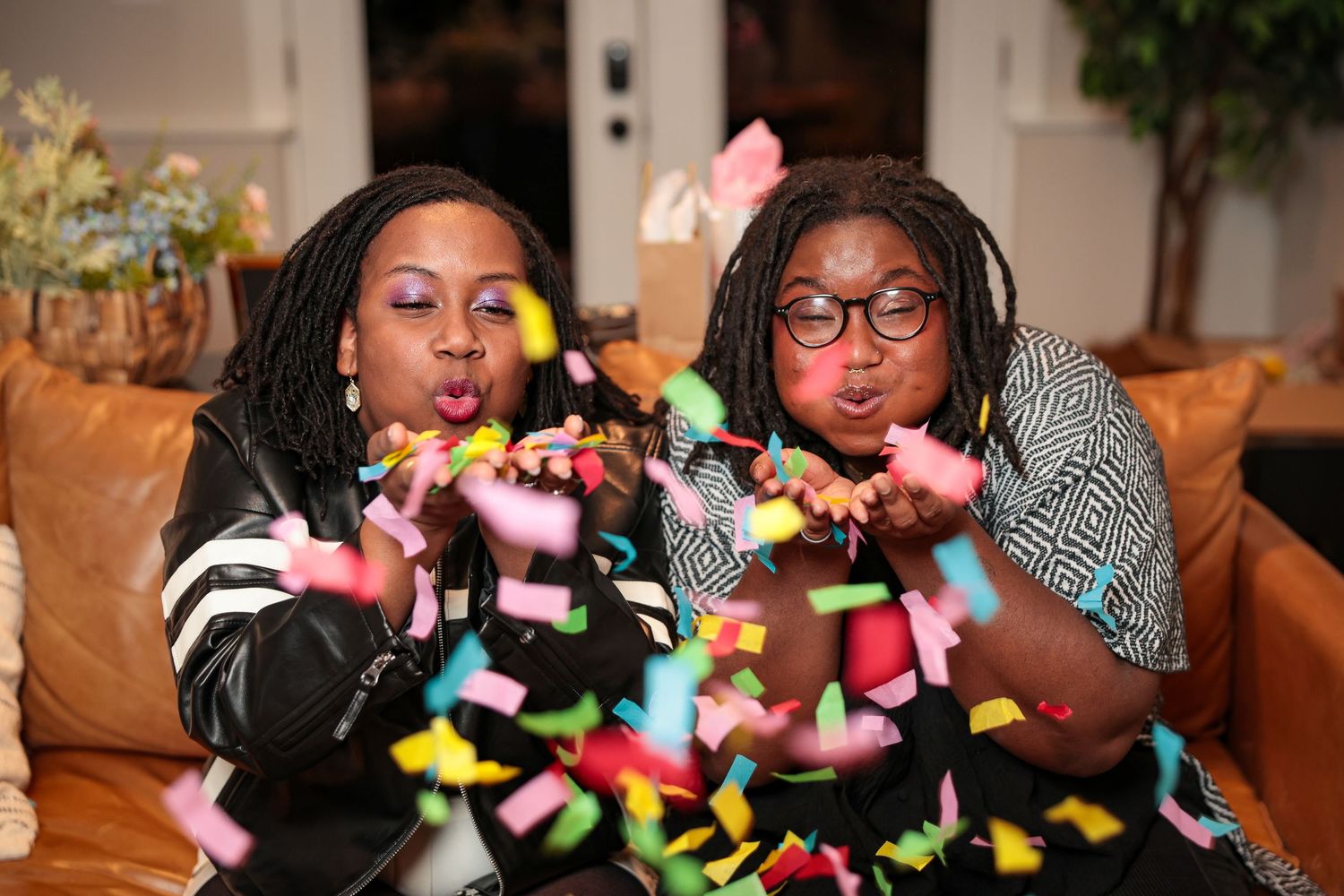 Friends laughing and playing with colorful confetti in an indoor setting.
