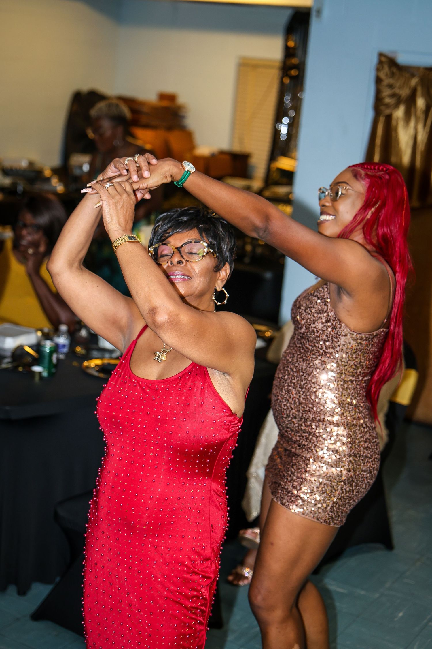 Dancers in sparkly red and bronze dresses move energetically on the dance floor during a party.