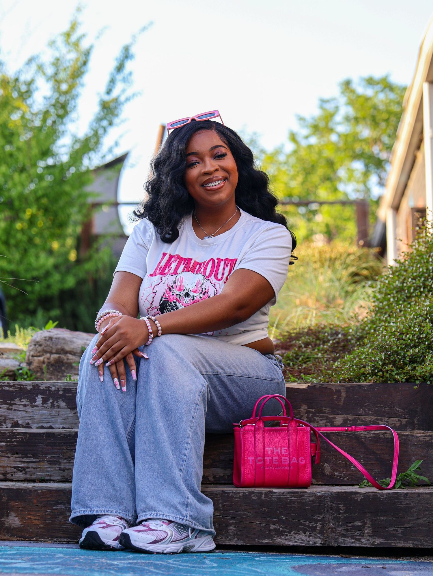 Lifestyle photography on wooden steps with bright pink accessories and casual summer outfit.