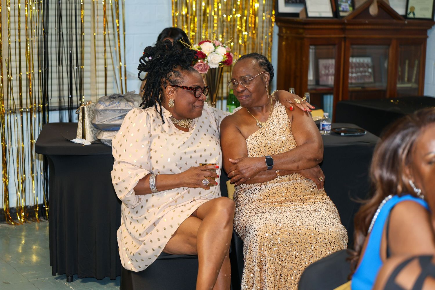 Partygoers in elegant outfits socialize and celebrate under gold party decorations.
