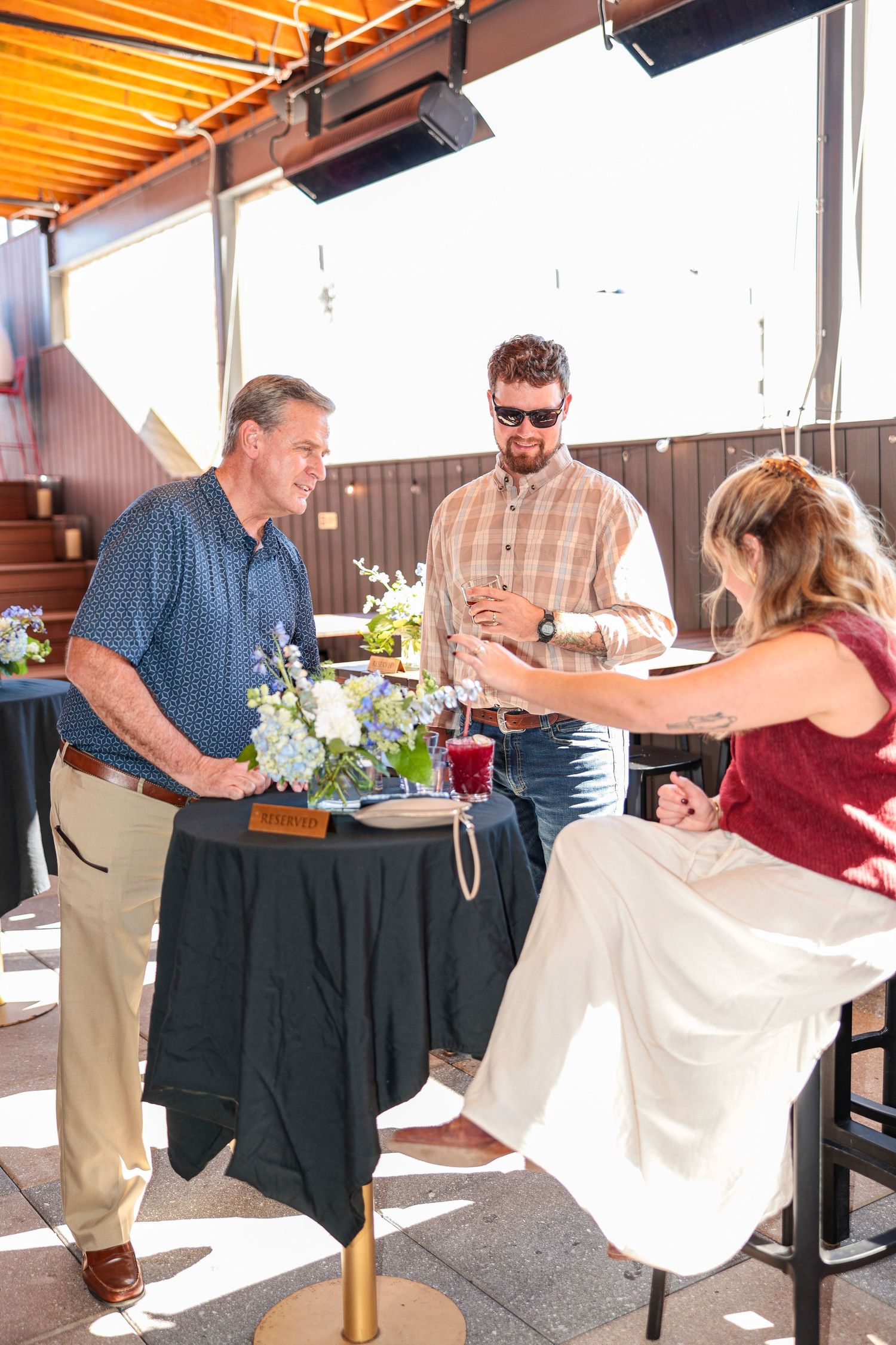 Guests interacting at tables with black tablecloths in a sunlit industrial venue.