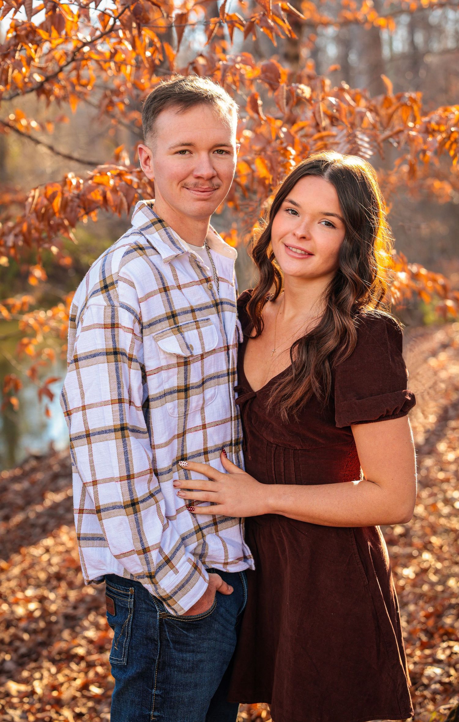 Couple poses together among fall foliage with warm autumn lighting.