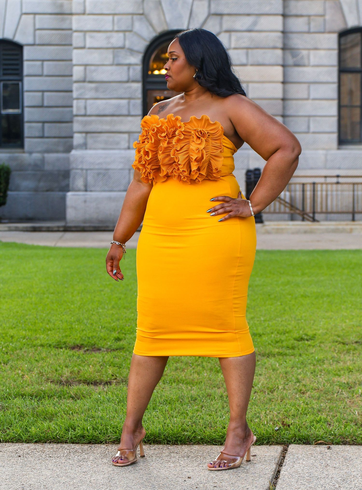 Fashion photography of a yellow dress with ruffles shown against architectural backdrop and lawn.