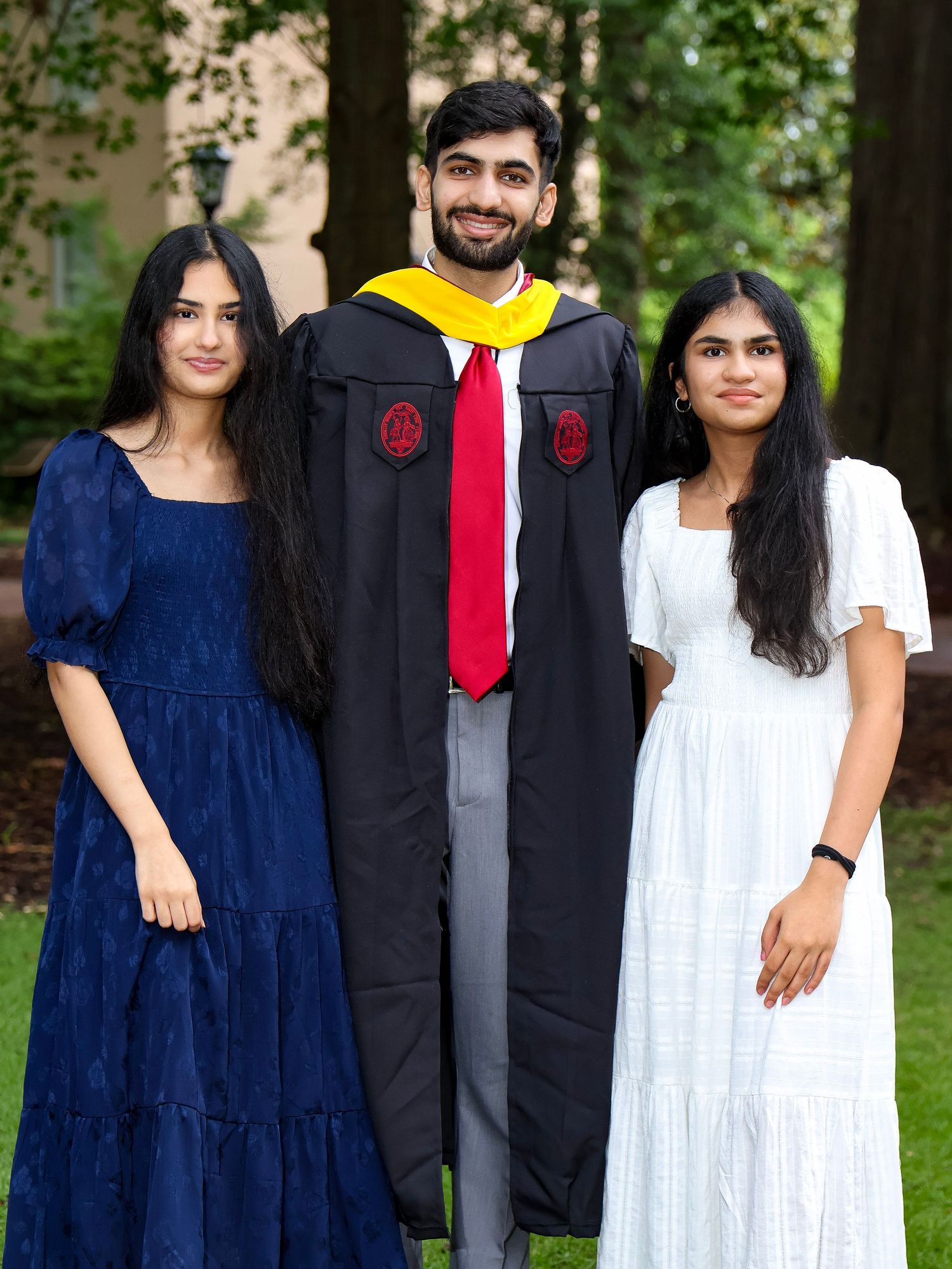 A graduate in black cap and gown poses with two companions in formal dresses.