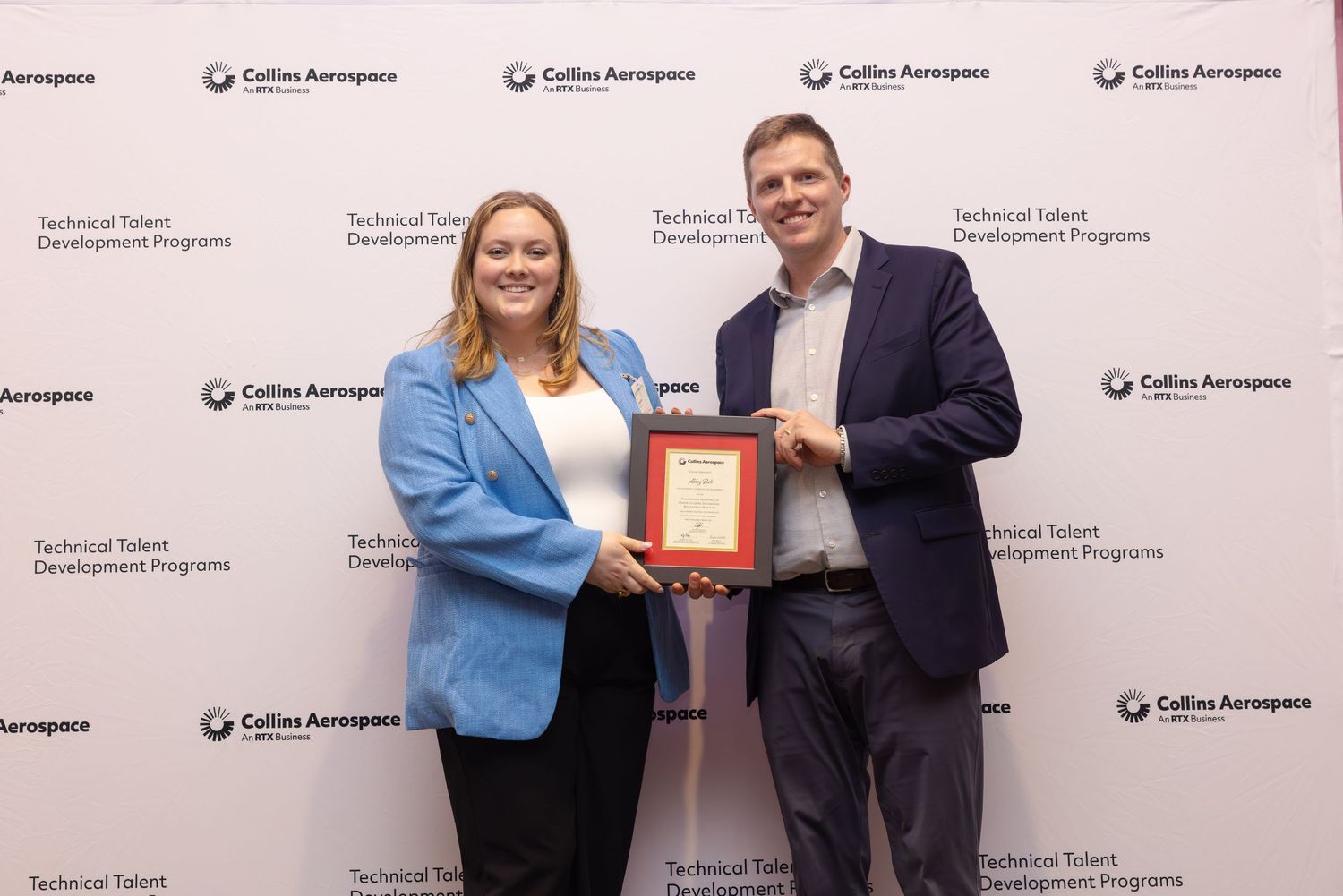 Two professionals pose together holding a framed award at a Collins Aerospace Technical Talent Development Programs event.