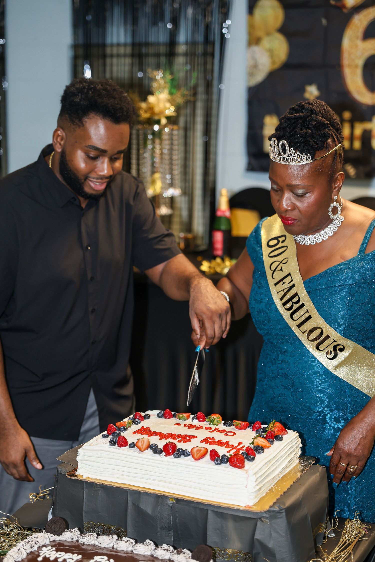 A celebration scene showing two people cutting a white birthday cake decorated with fresh berries.