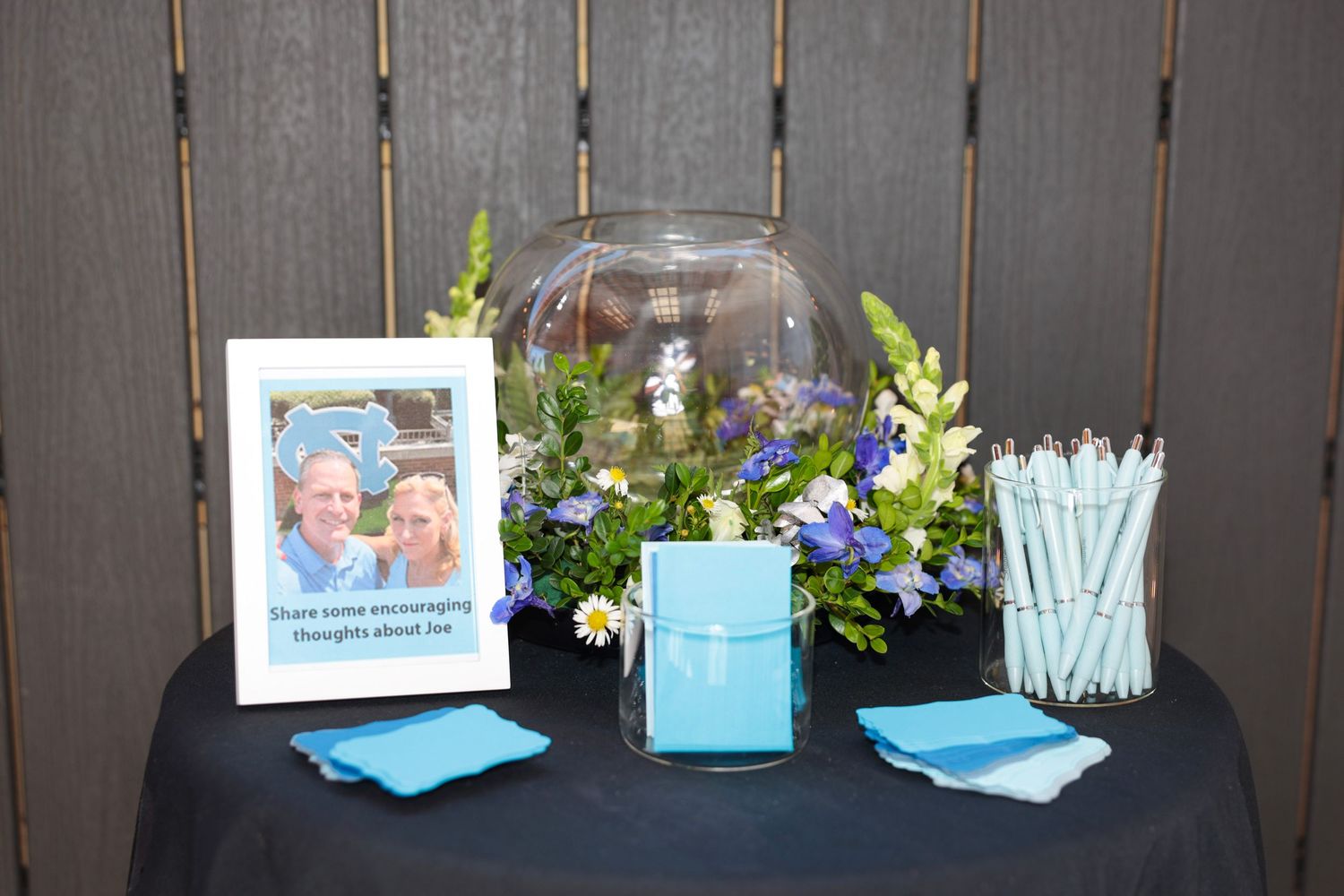 A decorative table display with a glass dome, blue flowers, and party supplies.