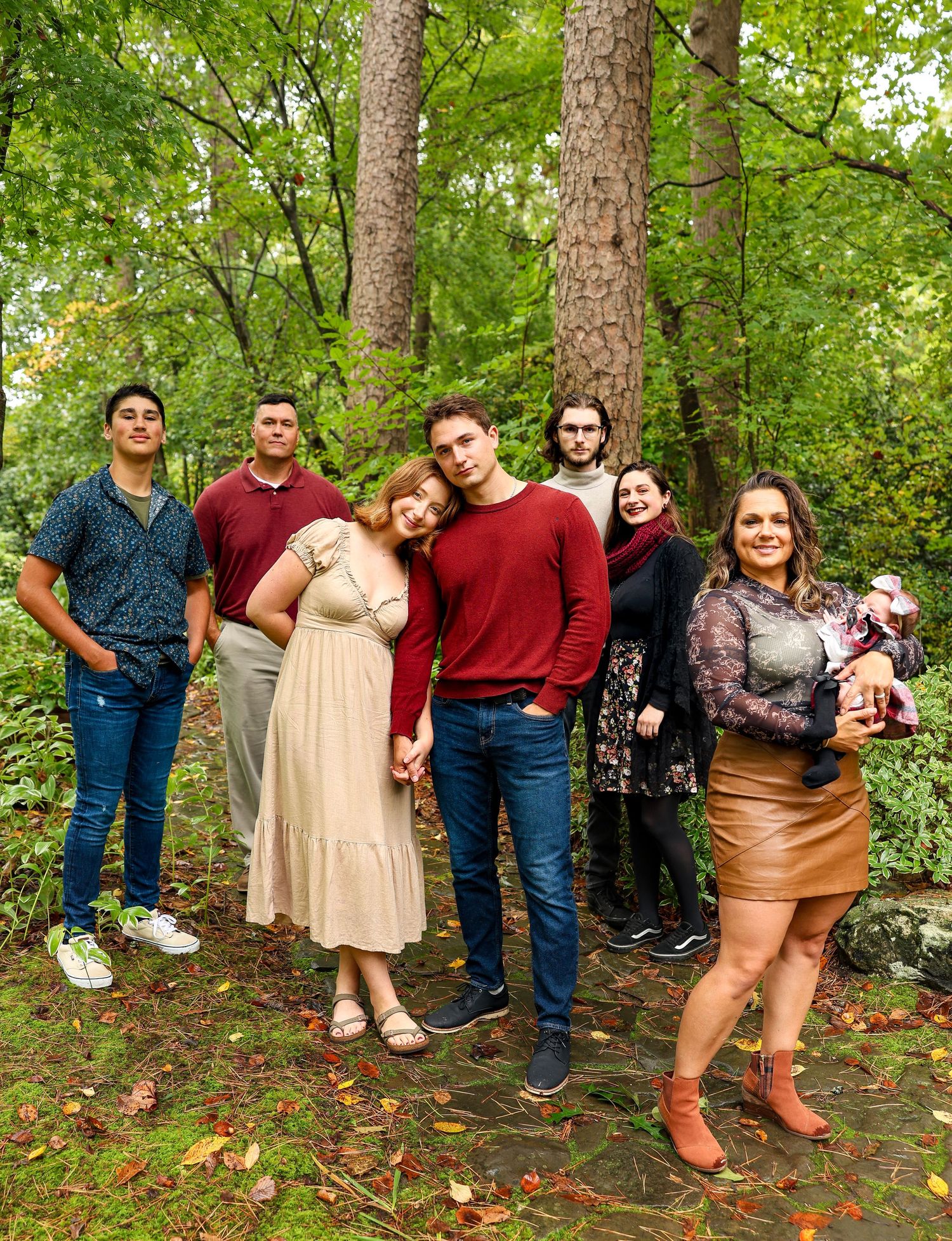 Group portrait of family members in casual attire standing among tall trees in wooded area.