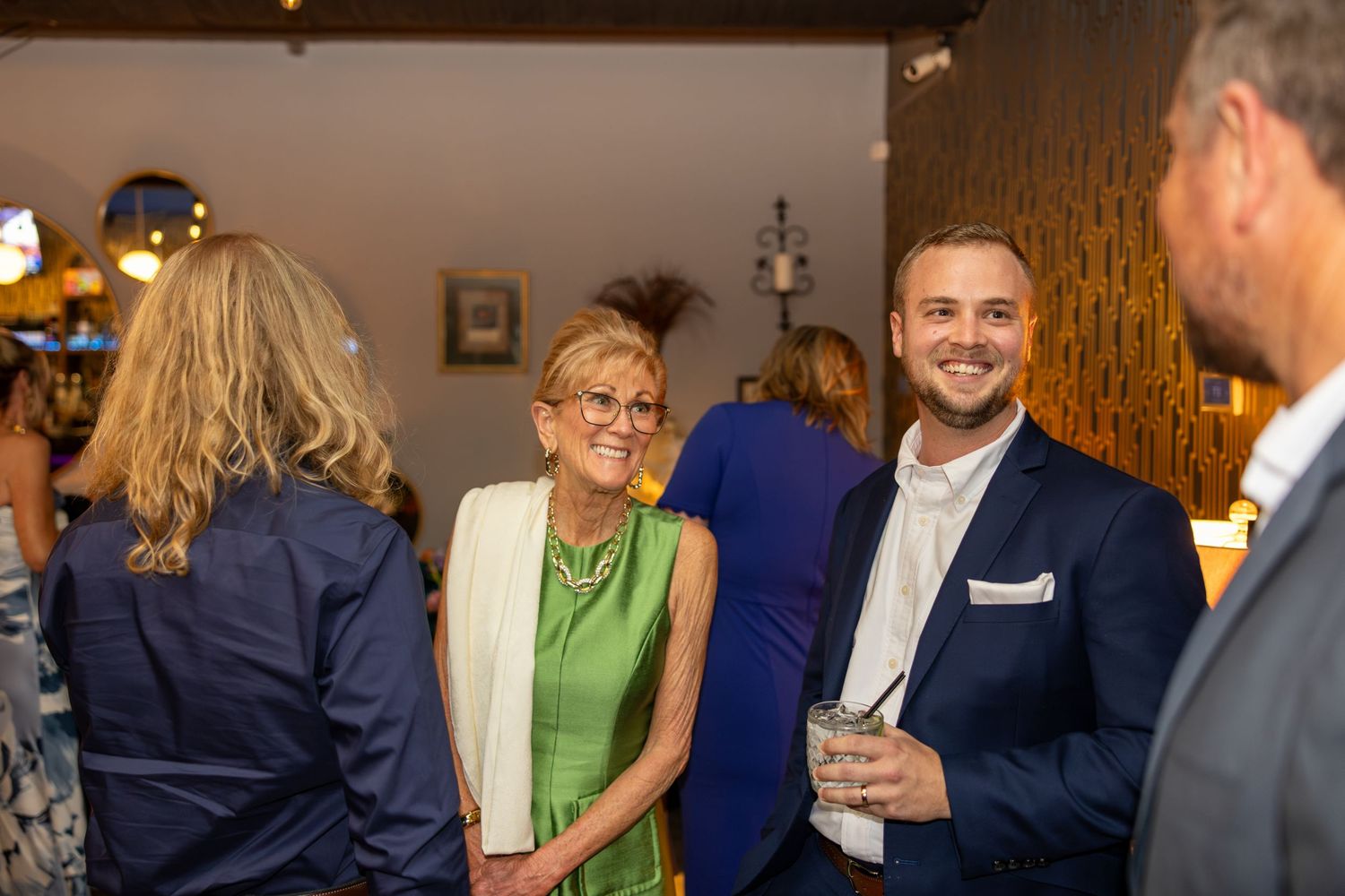 Guests networking at an elegant indoor social event, smiling and conversing in smart casual attire.
