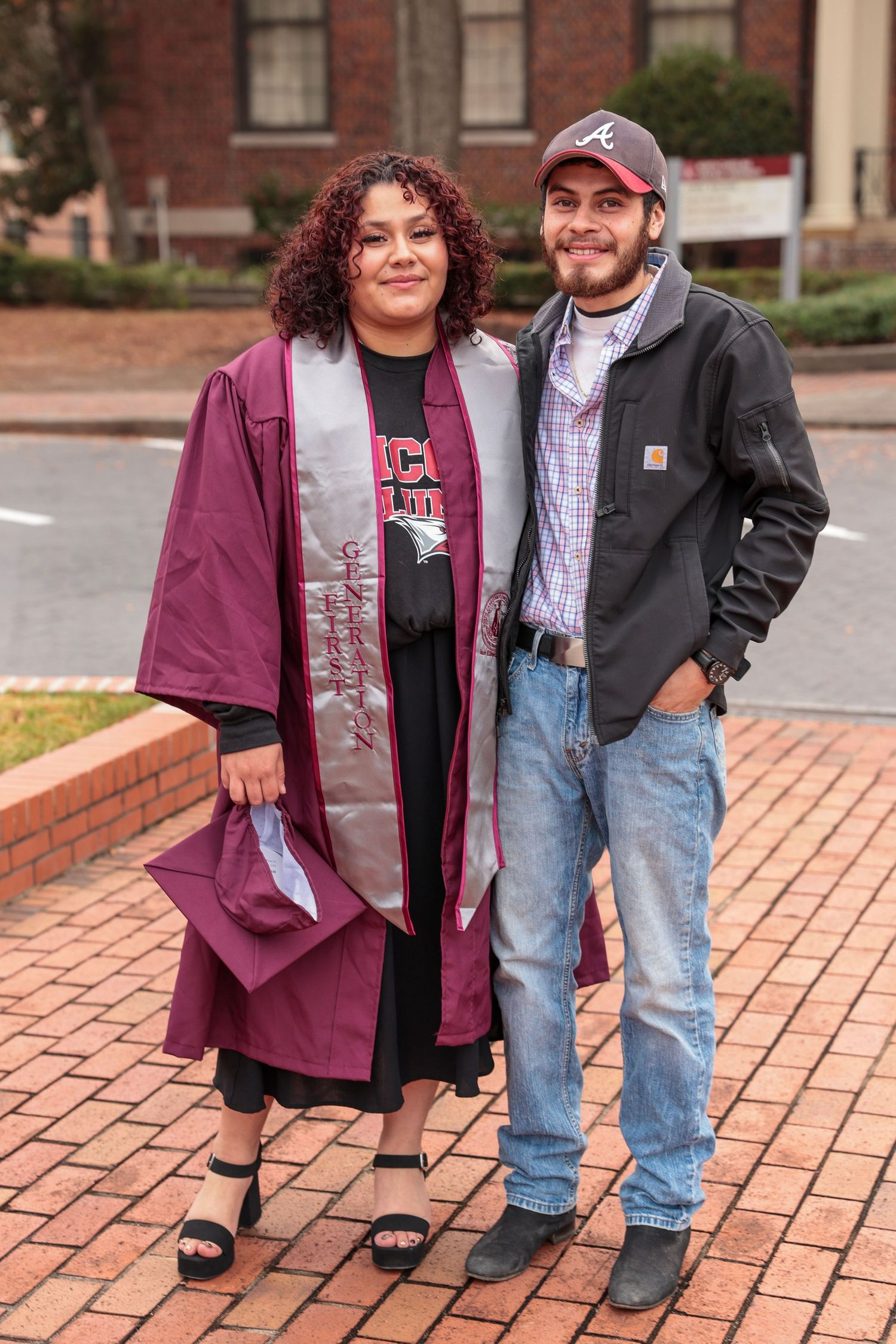 A couple posing together on brick pavement wearing casual attire.