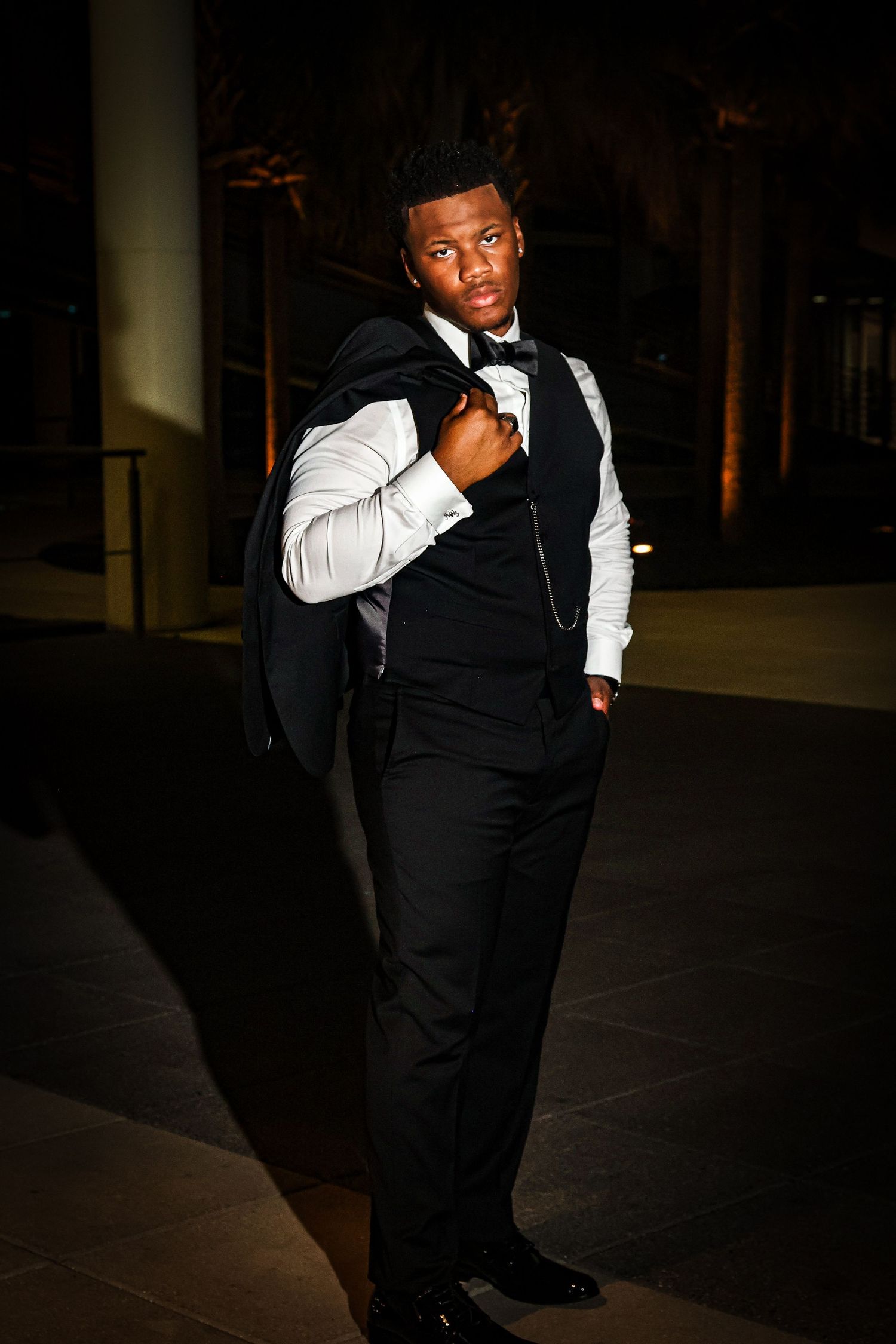 A person in formal wear creates dynamic poses in a moody, low-light setting.