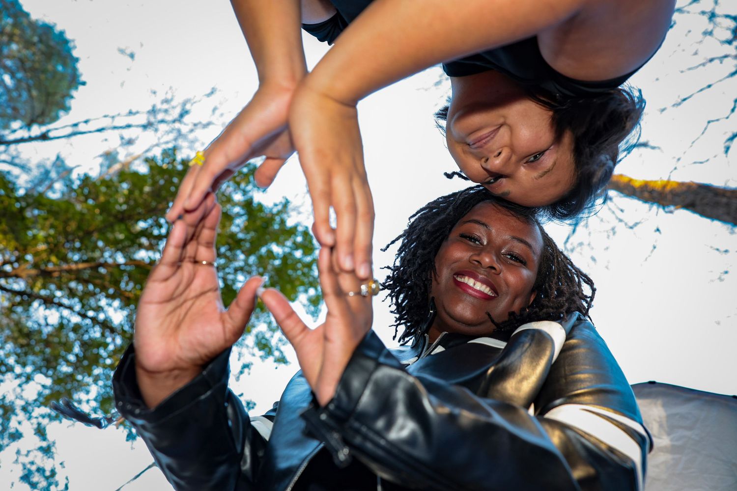 Low angle shot of friends reaching towards the camera against a blue sky background.