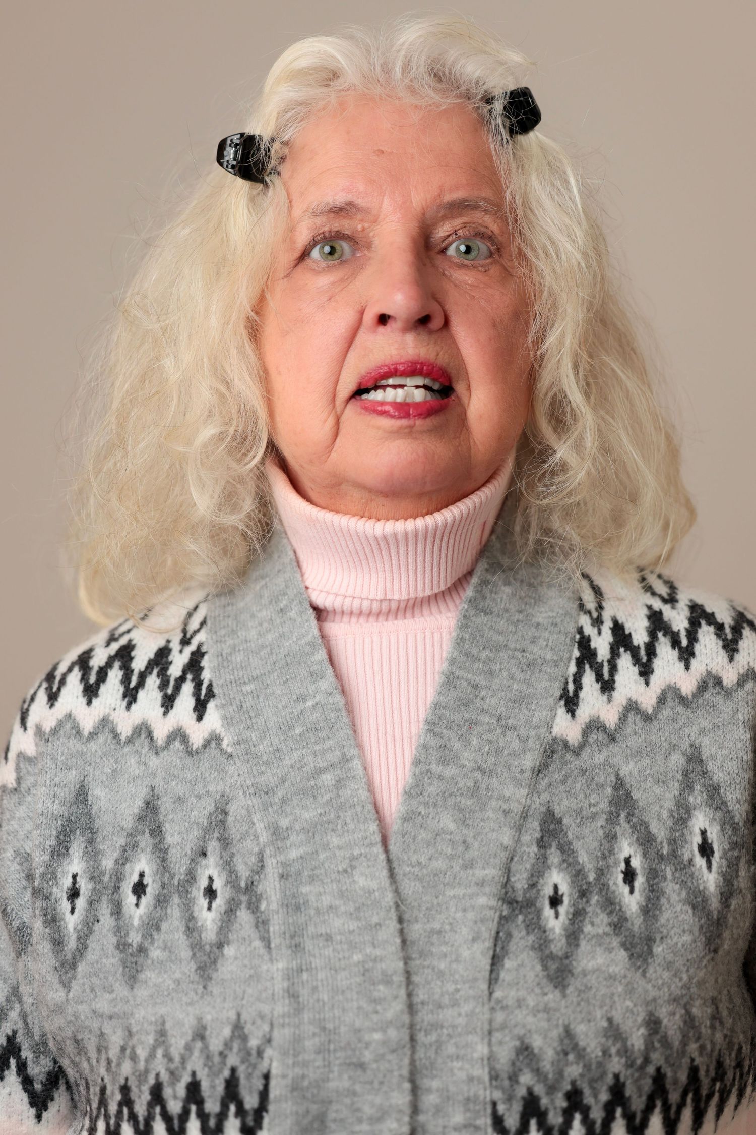 A person wearing a gray patterned sweater and pink turtleneck poses for a series of expressive headshots.