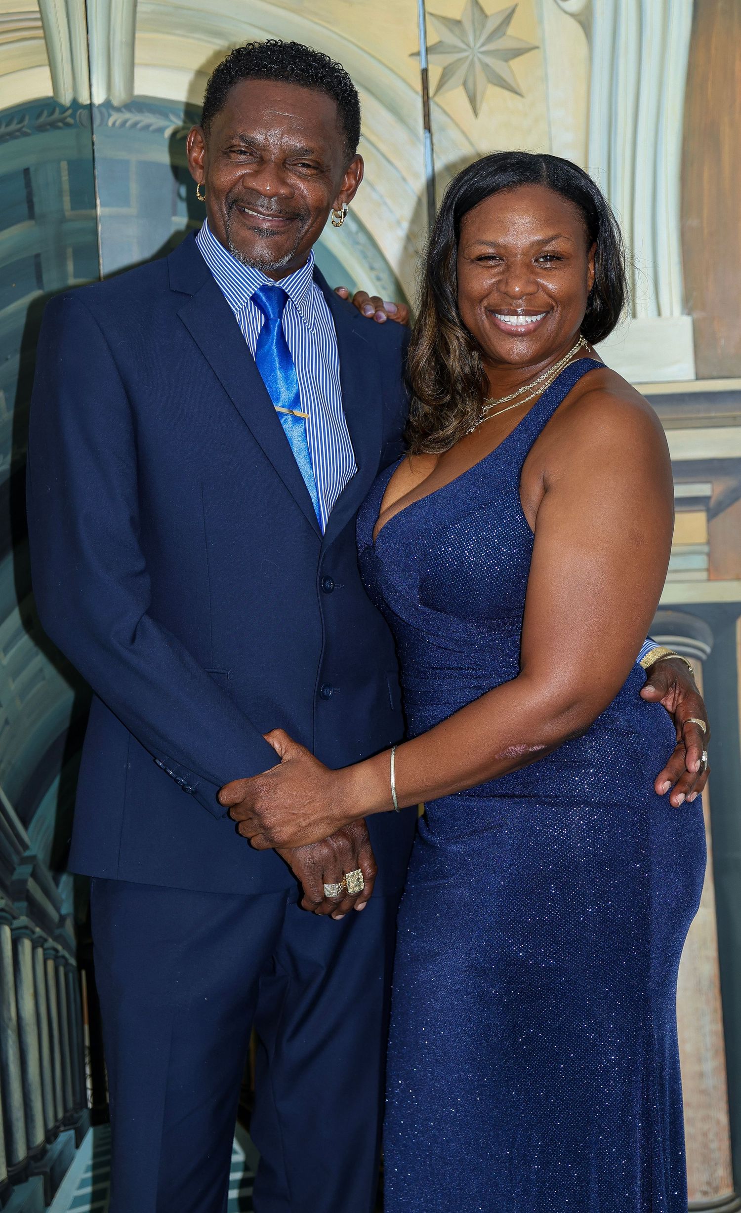 A formal portrait of two people in evening wear, with a man in a blue suit and woman in a navy gown.