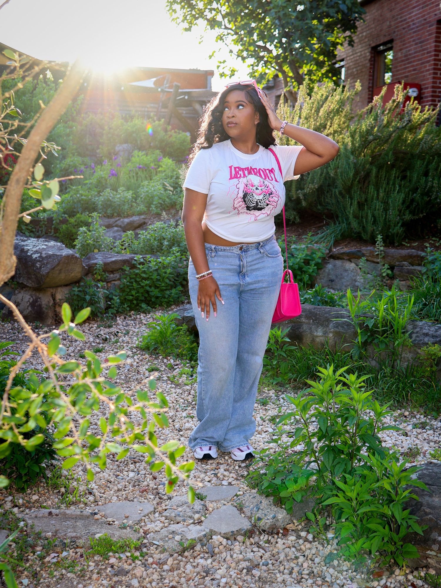 Casual outdoor photoshoot in a garden setting with brick building and greenery in background.