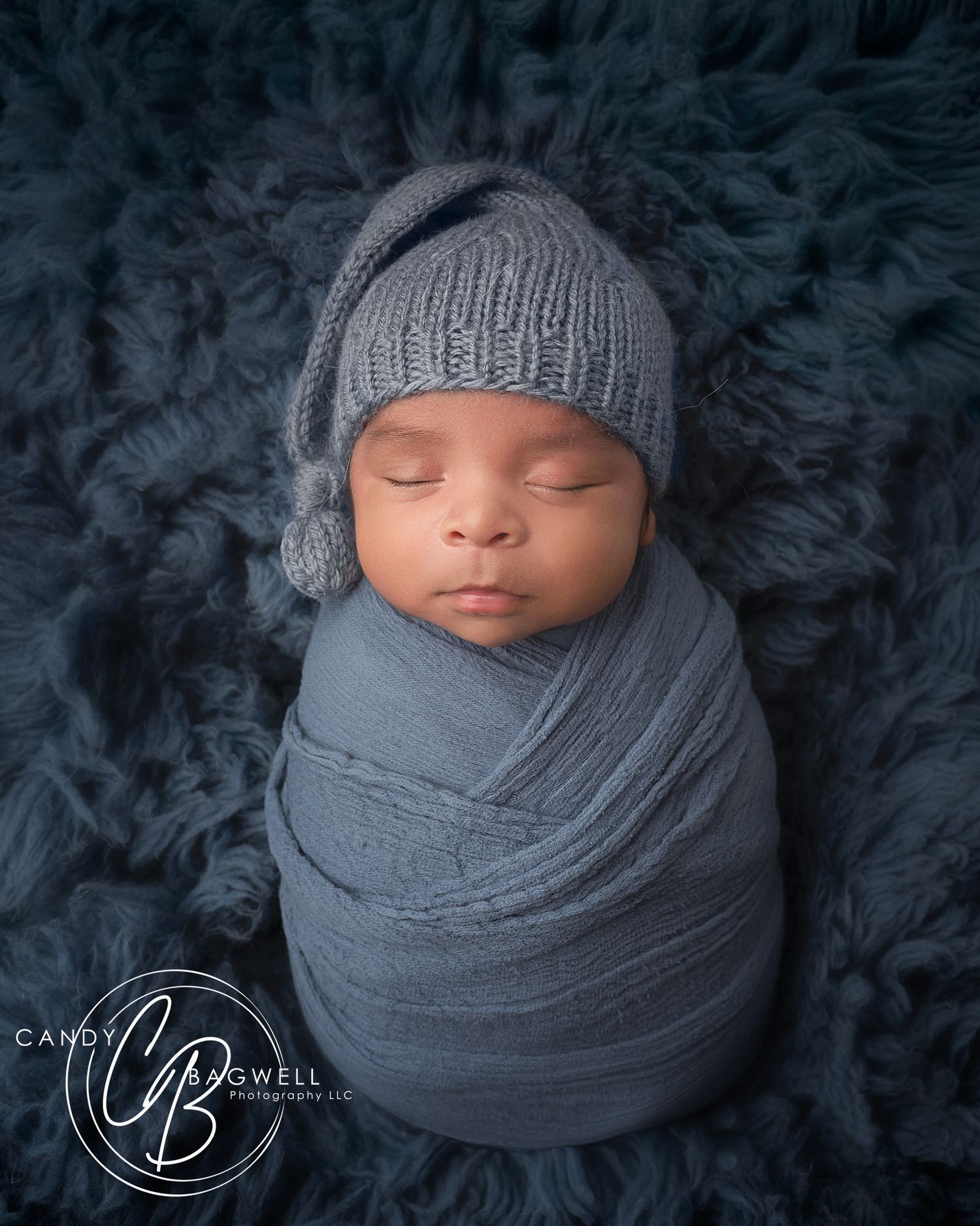 Newborn baby swaddled in gray wrap wearing knit hat sleeping on blue fur backdrop, professional newborn photography. Fletcher, Asheville.