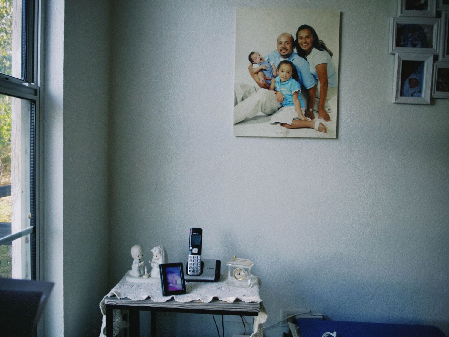 Family portrait hanging on wall above small table with phone and figurines near window in cozy home interior.