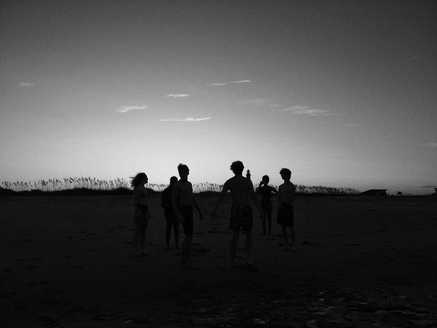 A series of black and white silhouettes against a horizon line shows people gathered outdoors at dusk.