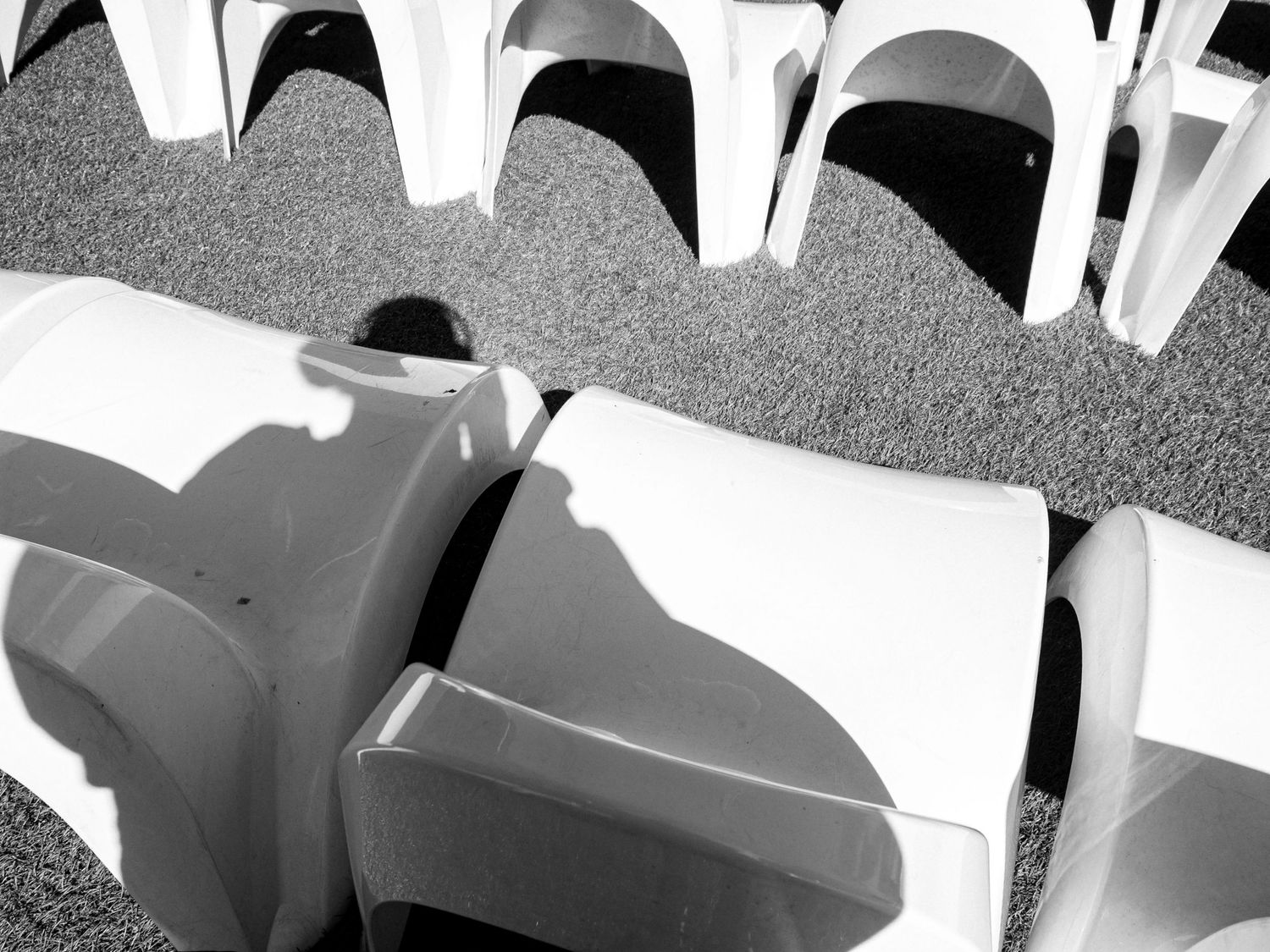 Black and white abstract view of empty stadium seats casting dramatic shadows on curved rows.