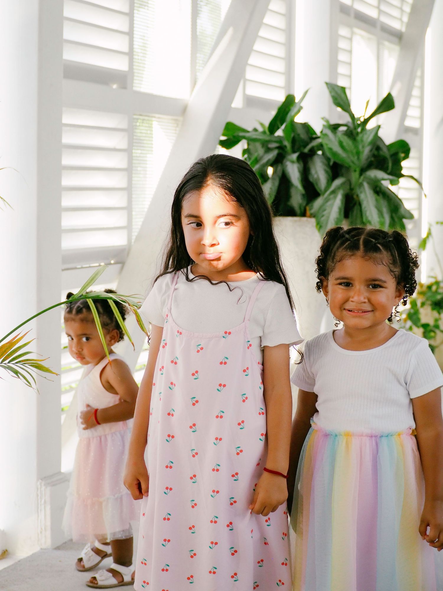 Children wearing white t-shirts and pastel tulle skirts pose playfully against a white shutter background.