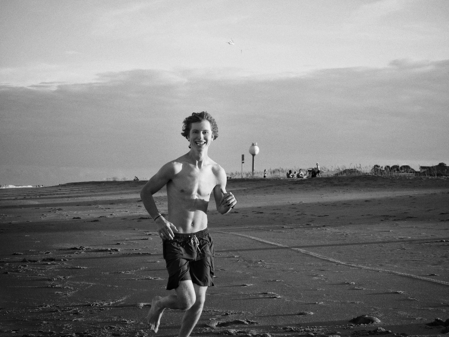 Black and white photograph of a person running on a beach at low tide with mountains in the distance.