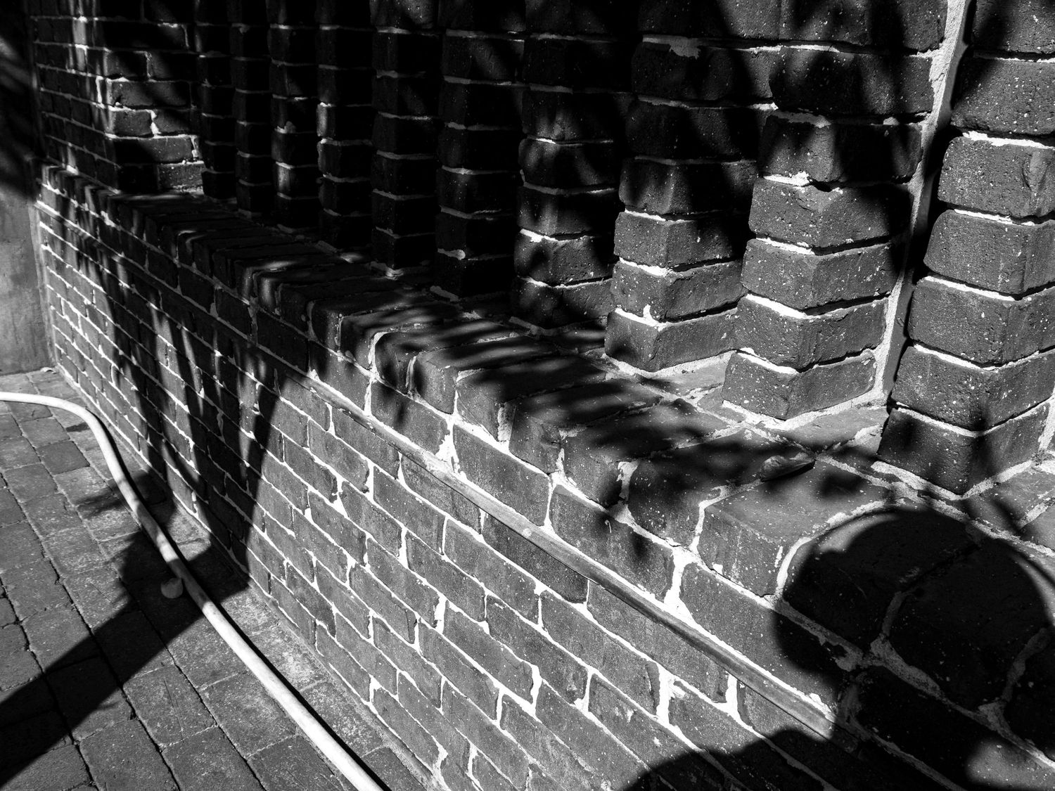 Dramatic black and white shadows cast on a brick wall create geometric patterns in harsh sunlight.