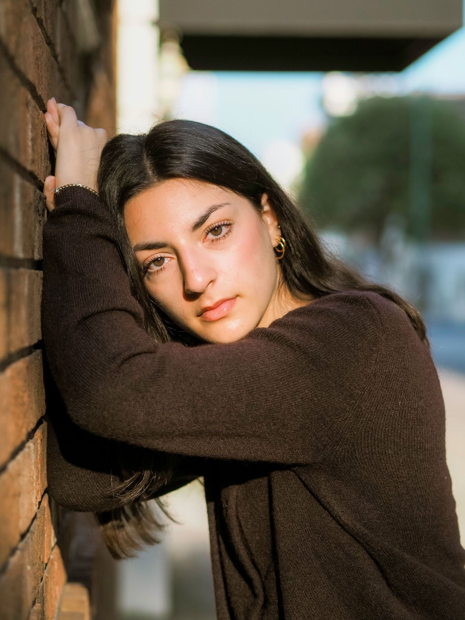 A person in a dark sweater poses against a brick wall in warm sunlight creating moody portrait shots.
