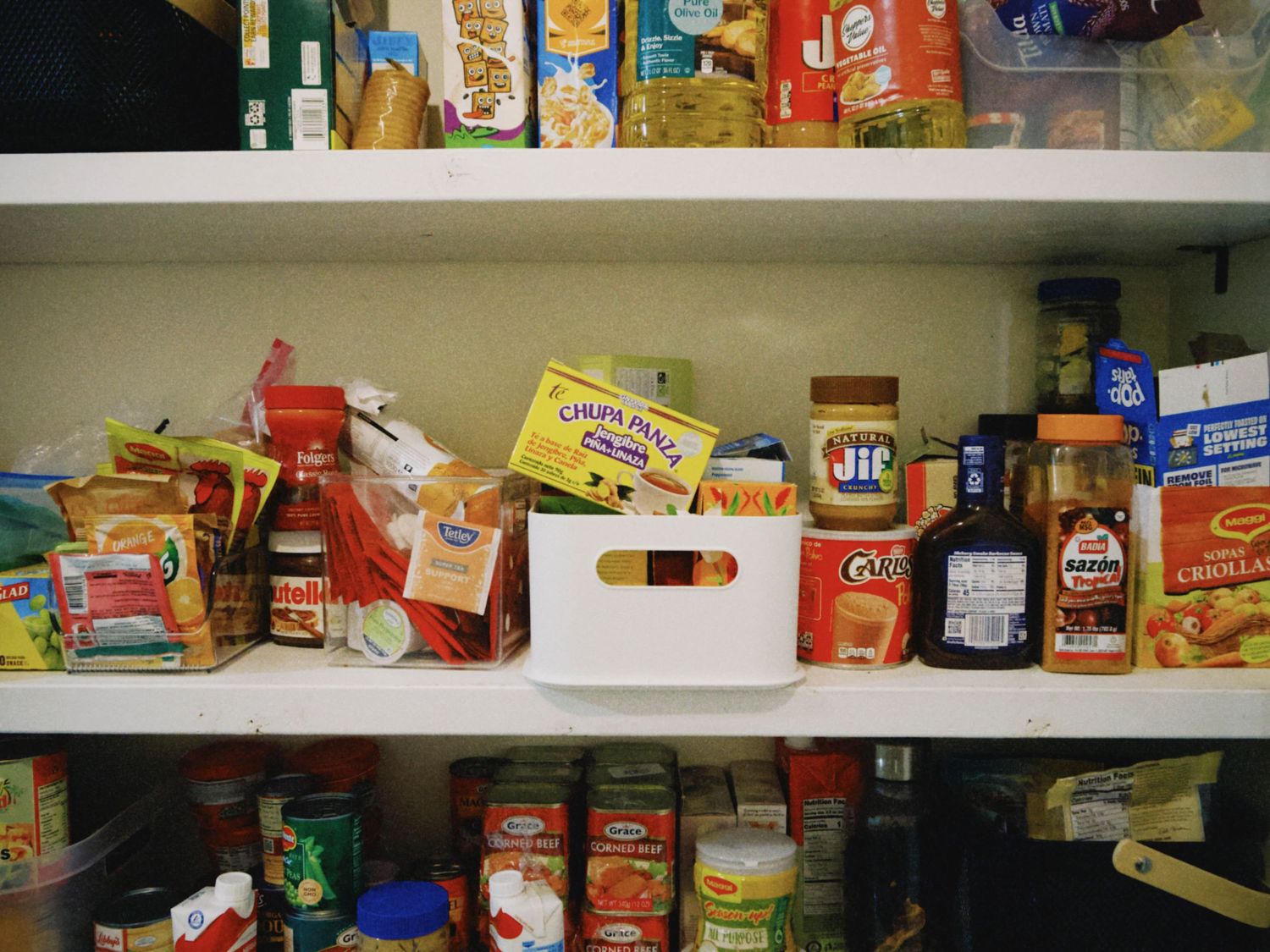 Pantry shelves stocked with Jif peanut butter, sauces, canned goods, and assorted food items in a home kitchen.