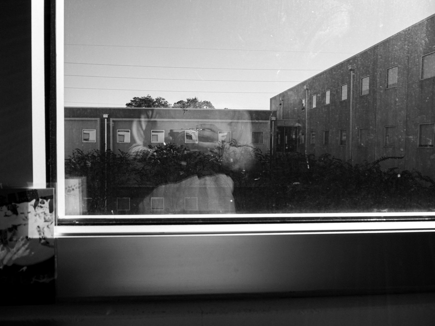 Black and white view through a window showing industrial buildings and reflections in the glass pane.