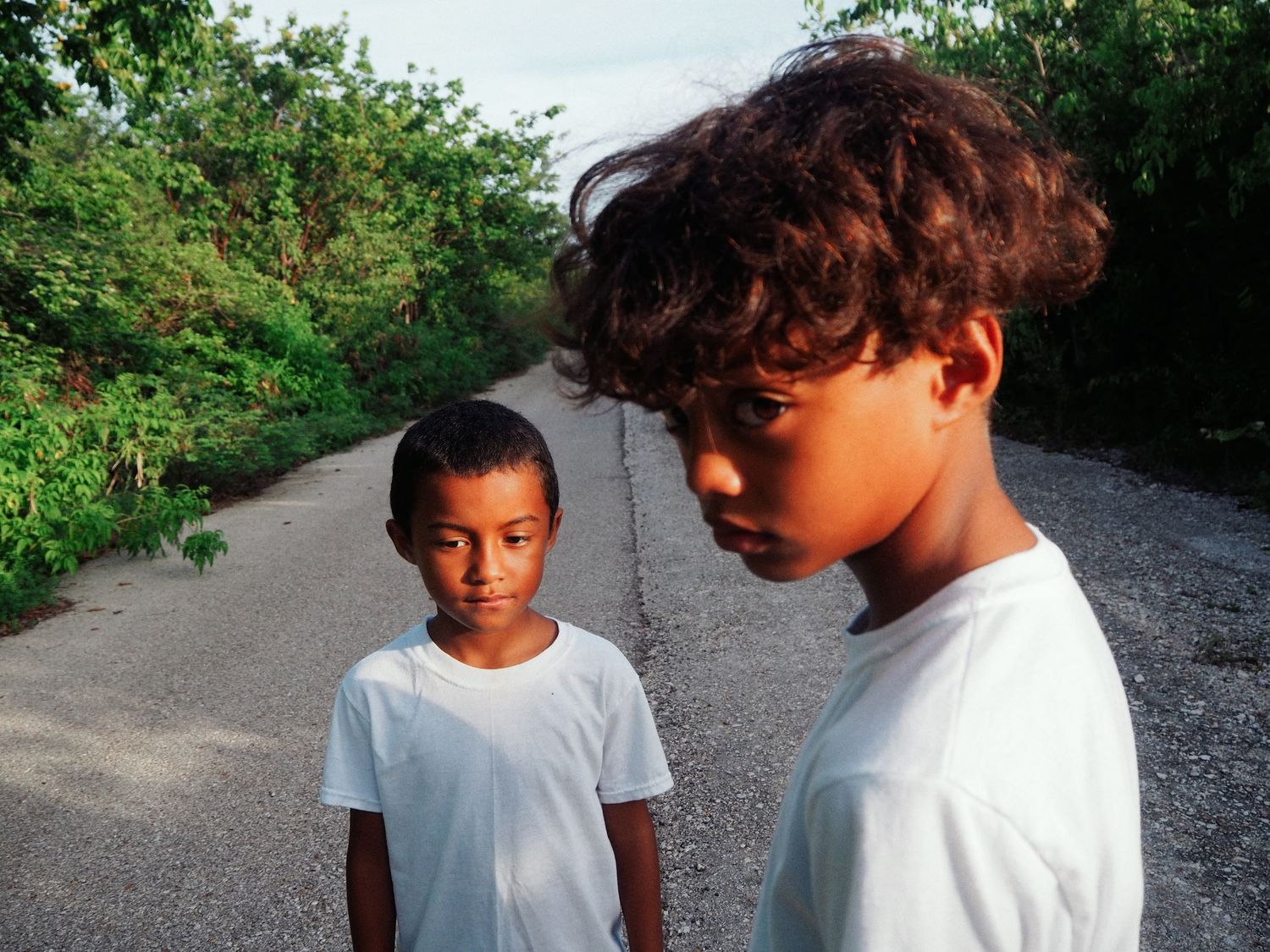 Two children walking together on a gravel path surrounded by lush green foliage.