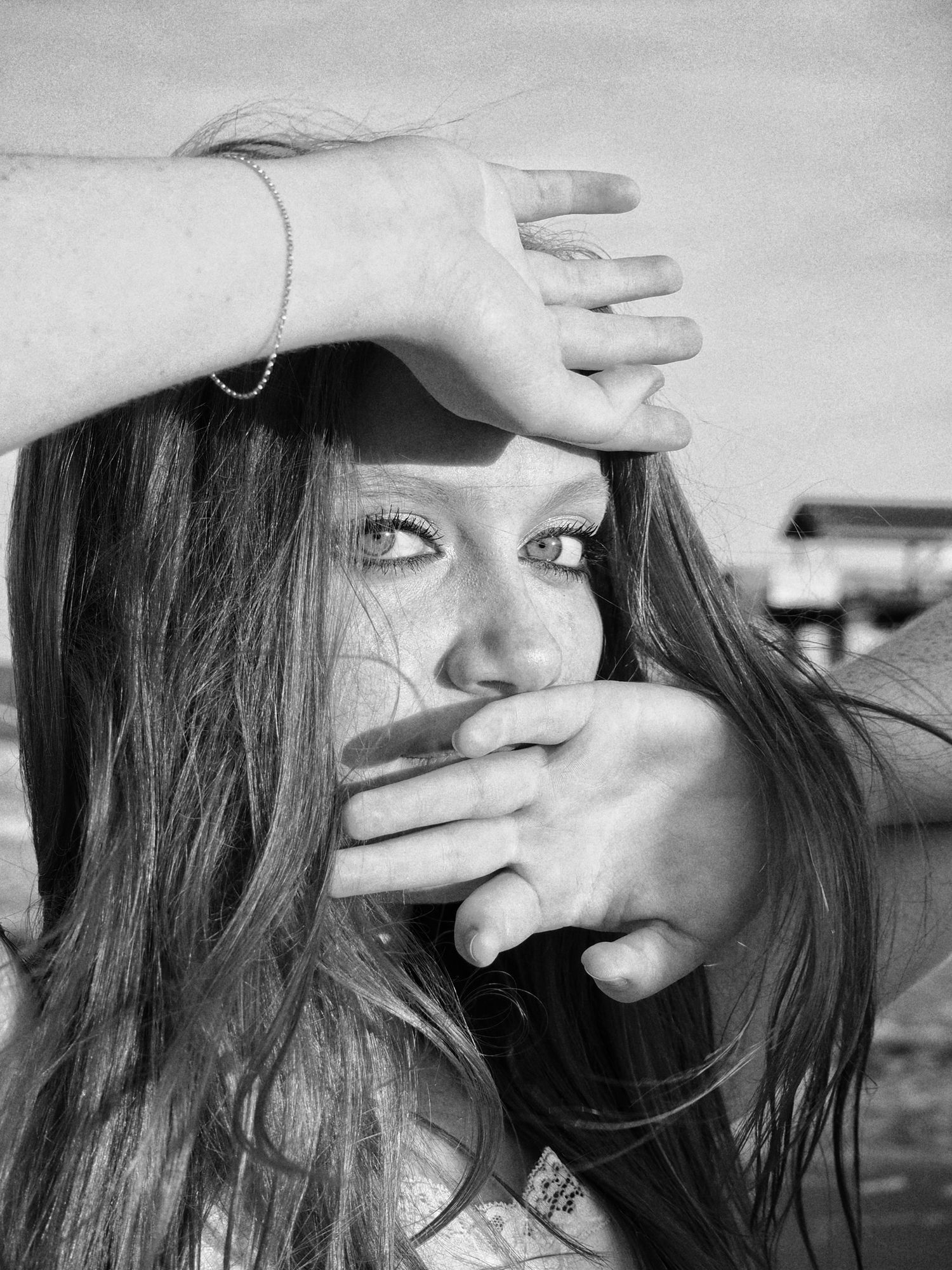 Black and white portrait of someone with long dark hair covering their mouth and forehead with their hands.